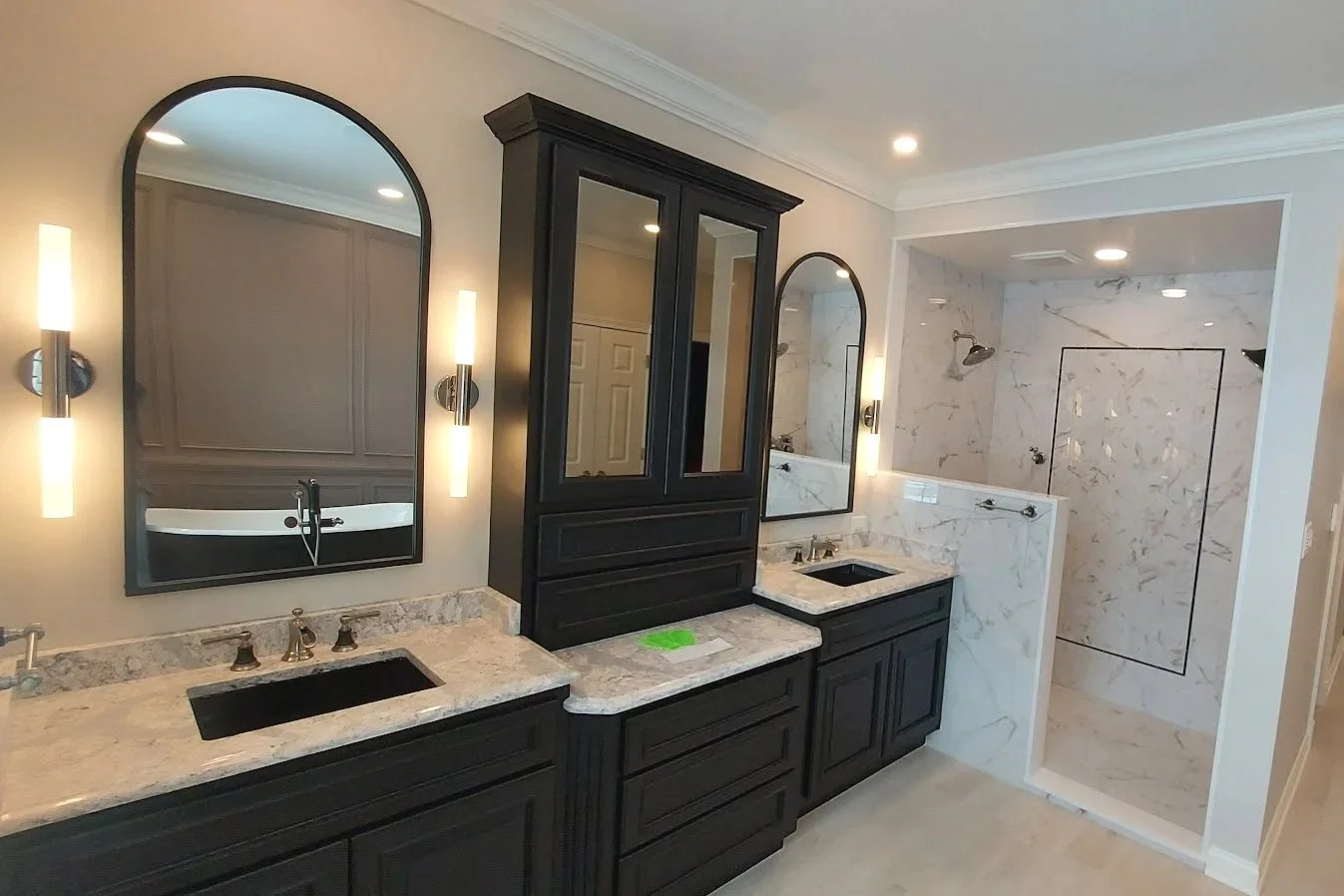 Bathroom with two single sinks, attractive mirrors, dark cabinetry, and a marble shower with glass door and wall panels.
