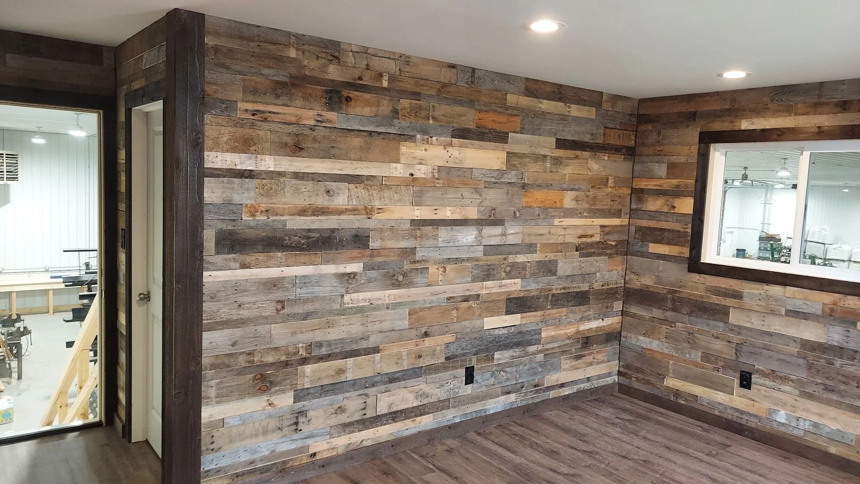 Interior corner of a room with wood-paneled walls and wood flooring, featuring a window and a door leading to another room.