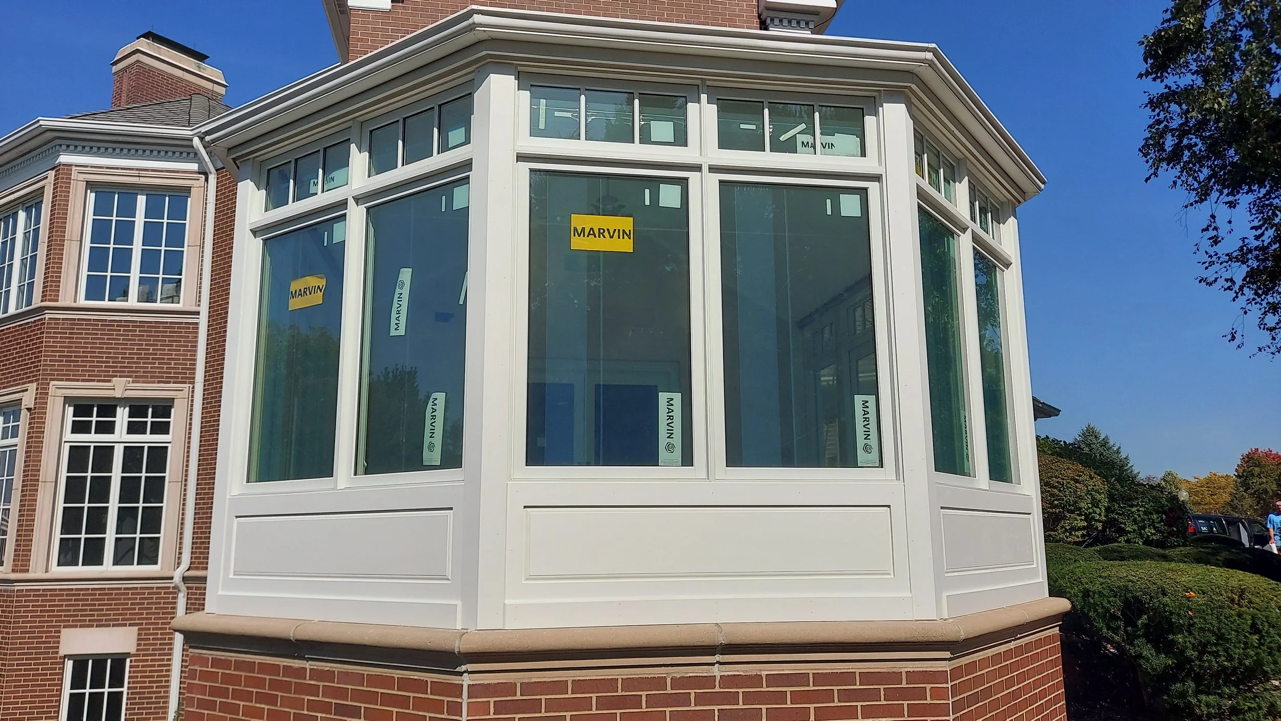 Newly constructed porch with white framing and large glass windows, with stickers that say 'Marvin,' attached to the glass.
