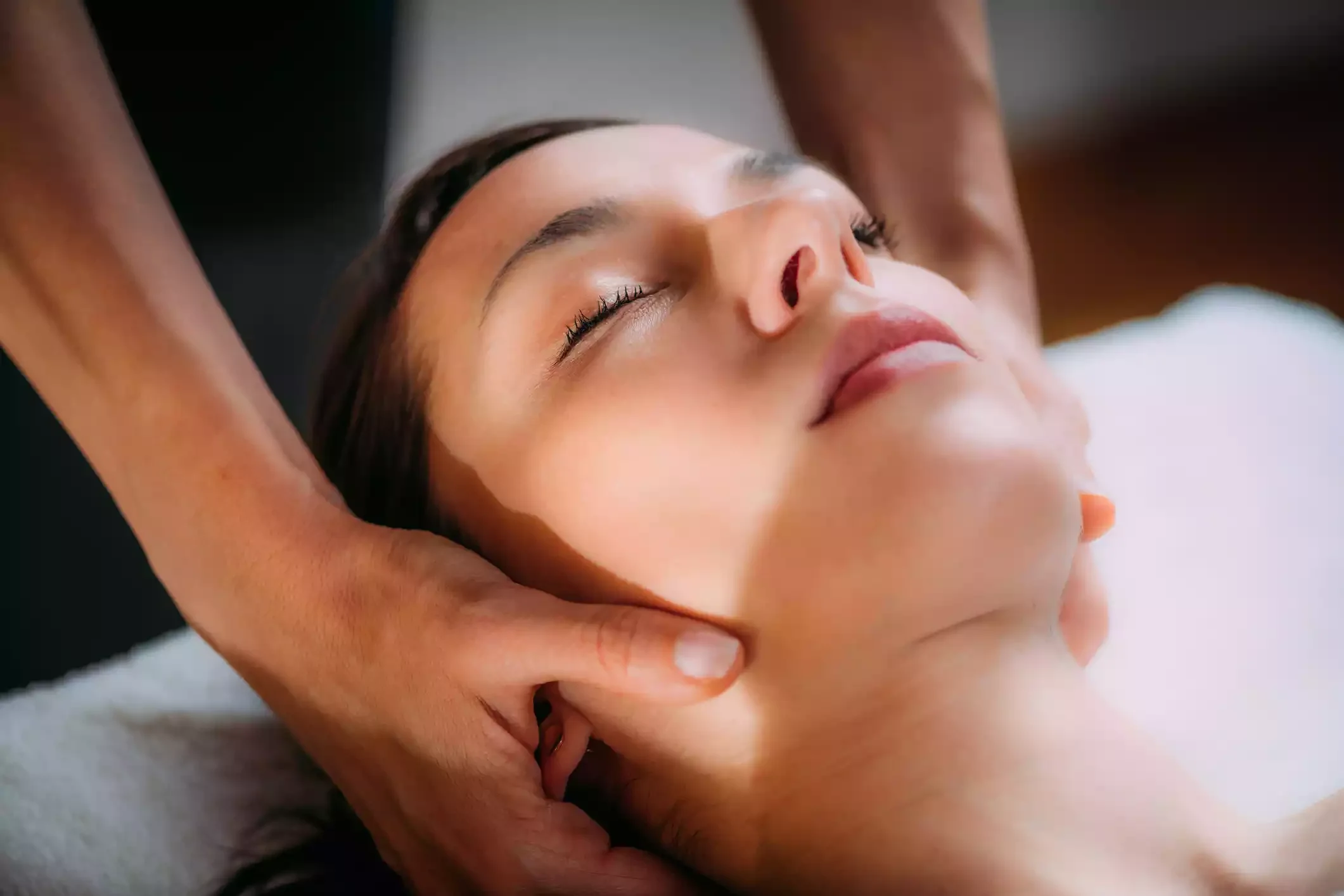 A female patient, relaxed with eyes closed, receives a cranial osteopathic procedure.