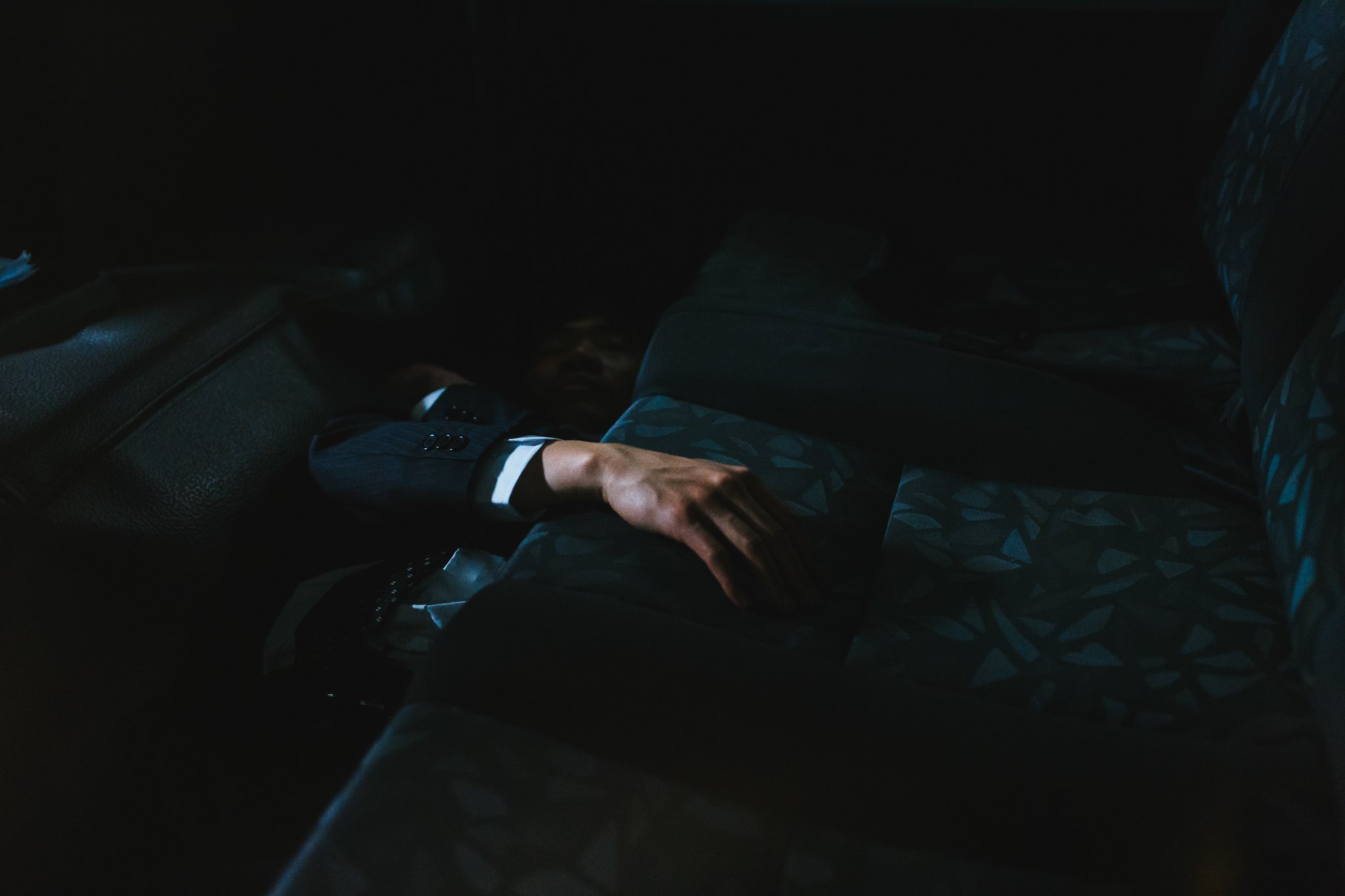 Person lying in the backseat of a car in dim lighting with a hand visible on the seat.