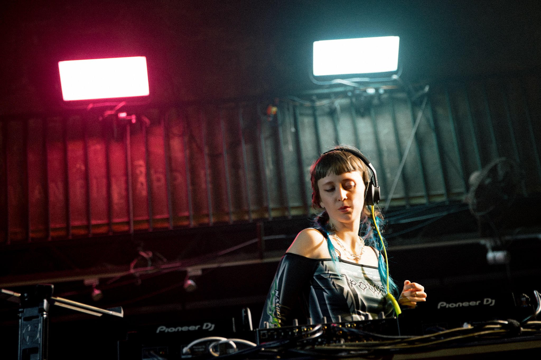 DJ performing in a dimly lit club with headphones, illuminated by colorful lights.