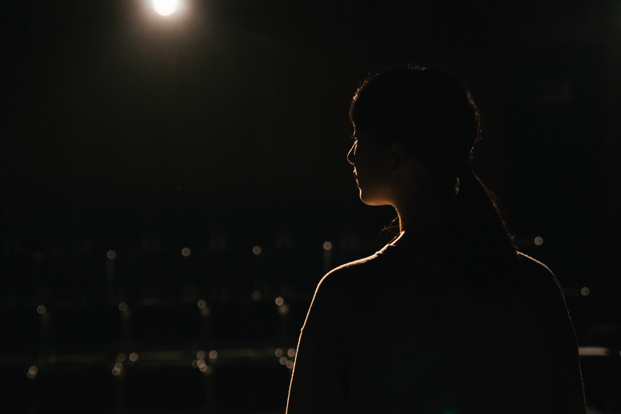 Silhouette of a woman on a dimly lit stage with spotlight overhead.