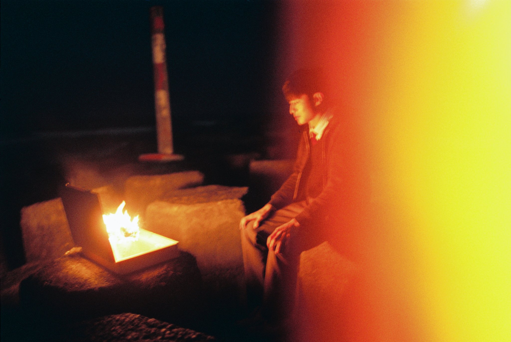 Person sitting near a suitcase with fire at night