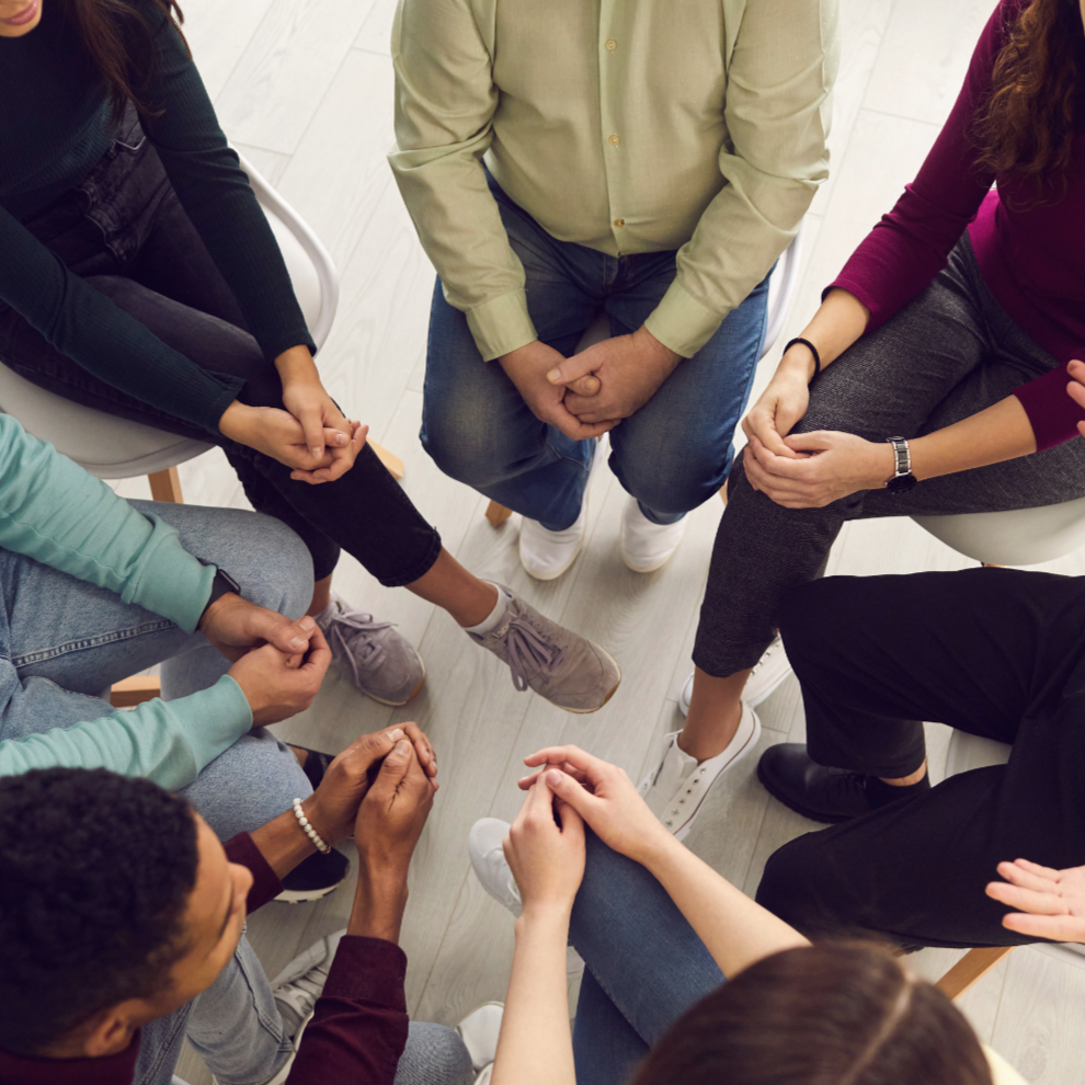 People sitting in a circle holding hands, participating in a group activity or prayer.