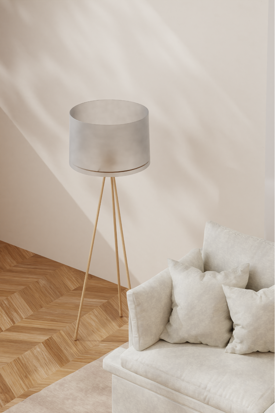 A modern white floor lamp with a cylindrical shade and three wooden legs, positioned next to a beige sofa with white pillows, in a minimalist living room with herringbone wood flooring and plain light-colored walls.