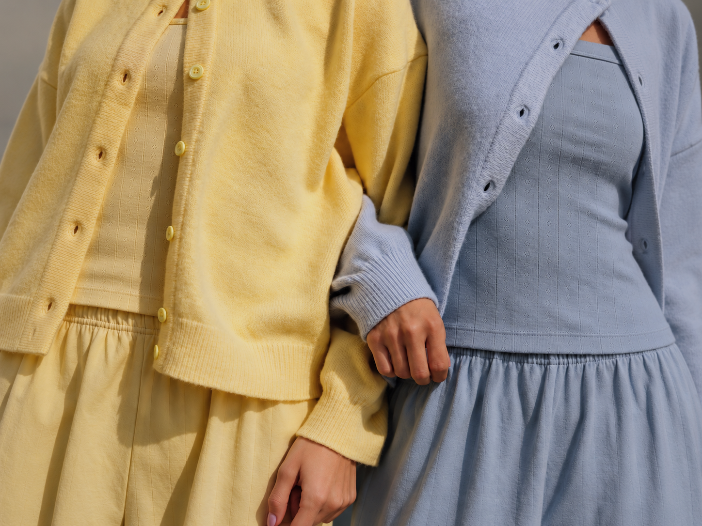 Two people standing arm in arm, wearing soft yellow and blue outfits.