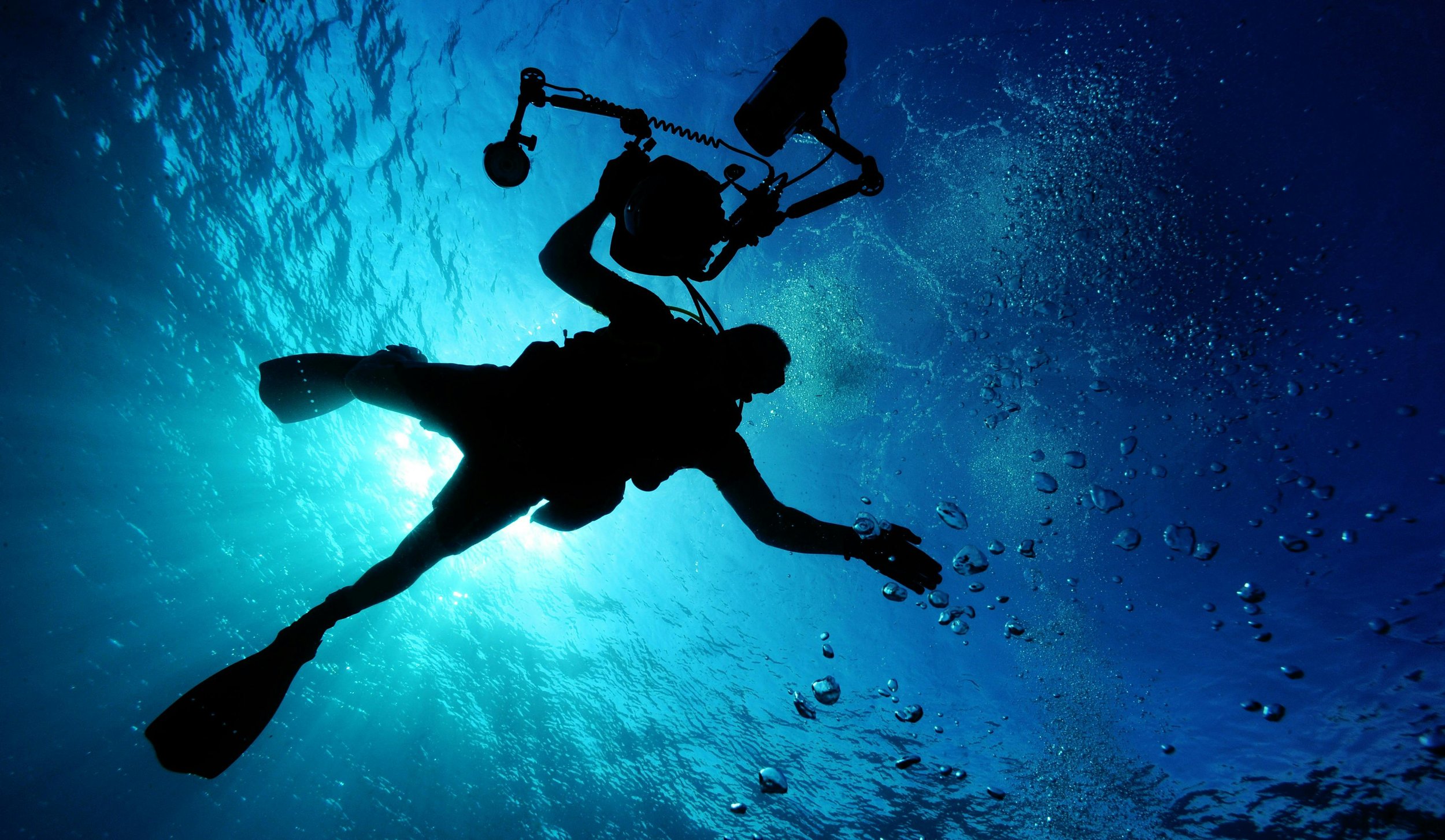 Silhouette of a scuba diver underwater with bubbles and blue water background.
