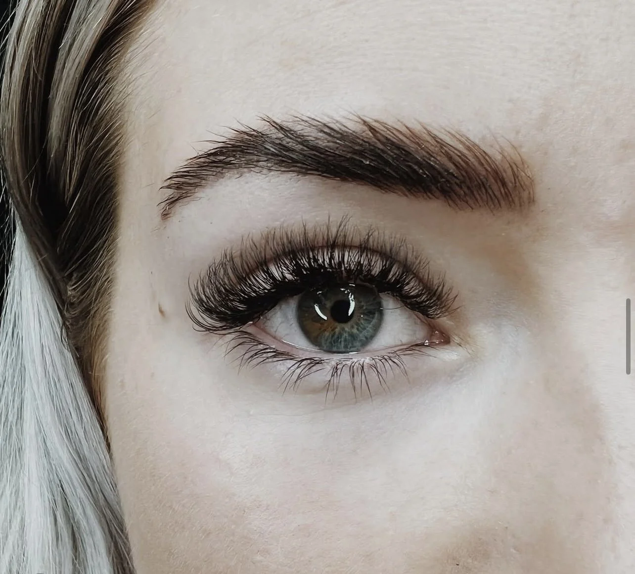 Close-up of a woman's eye with long eyelashes, well-groomed eyebrow, and eye makeup, with part of her hair visible on the left.