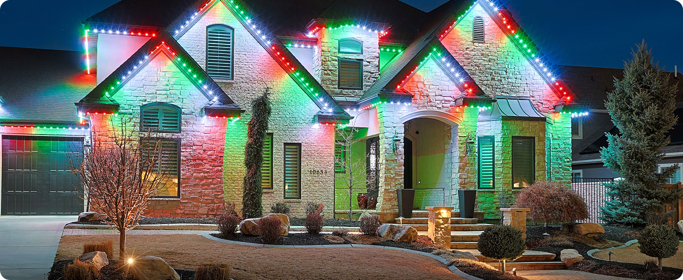 A house decorated with colorful holiday lights at night, with a well-maintained front yard and landscaping.