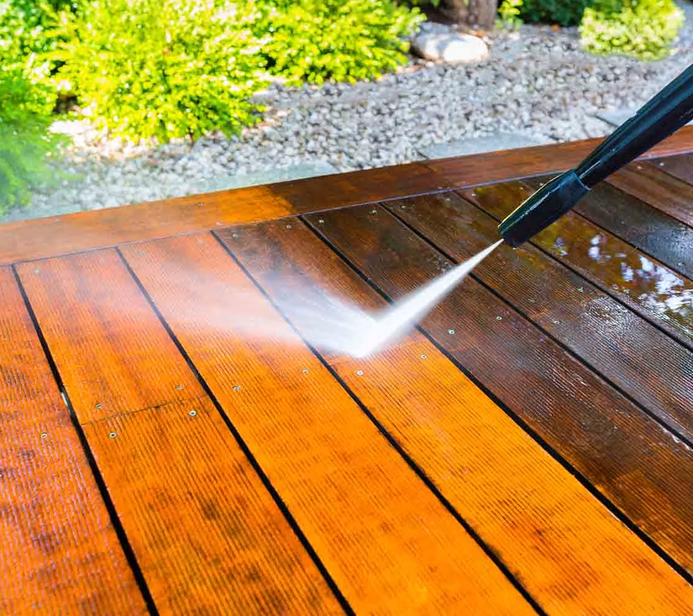 A pressure washing nozzle blasting a high-pressure stream of water across wooden deck boards, restoring the light natural wood color from a dark, weathered finish.