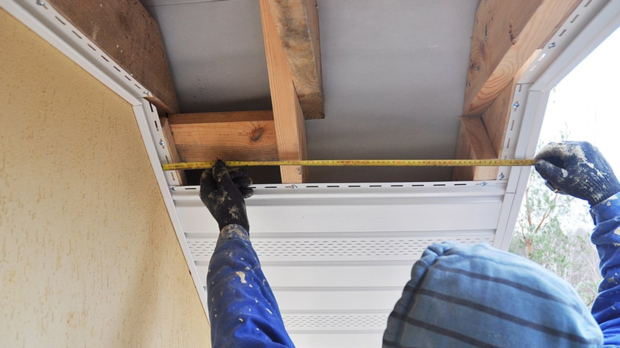 Person measuring the height of a wall or door frame with a tape measure during home construction or renovation.