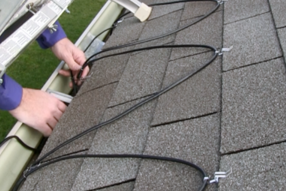 Person installing or repairing electrical wires on a house roof with shingled surface.