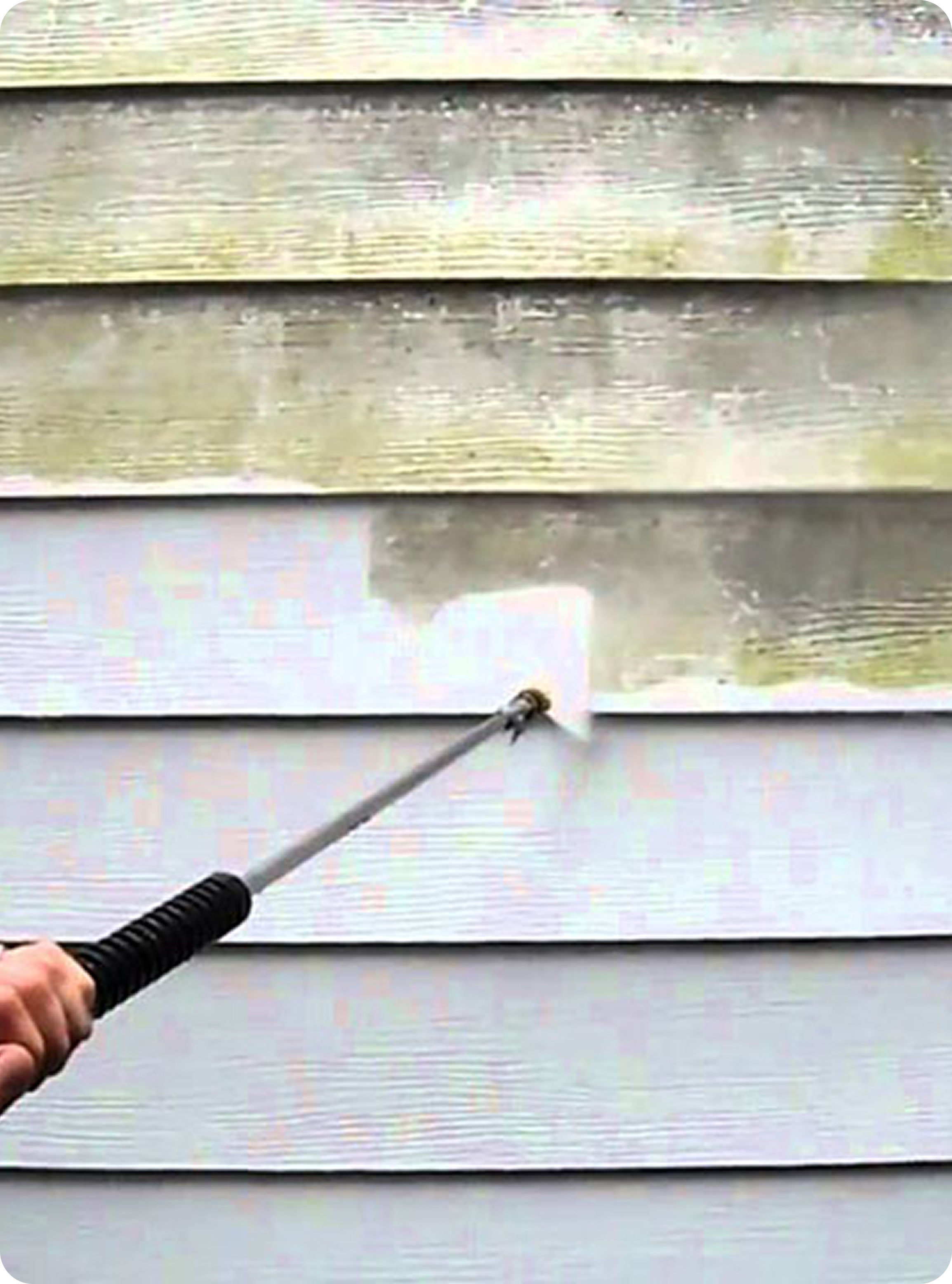 A close-up view of a pressure washer nozzle blasting dirty, discolored home siding with water, revealing clean white siding beneath.