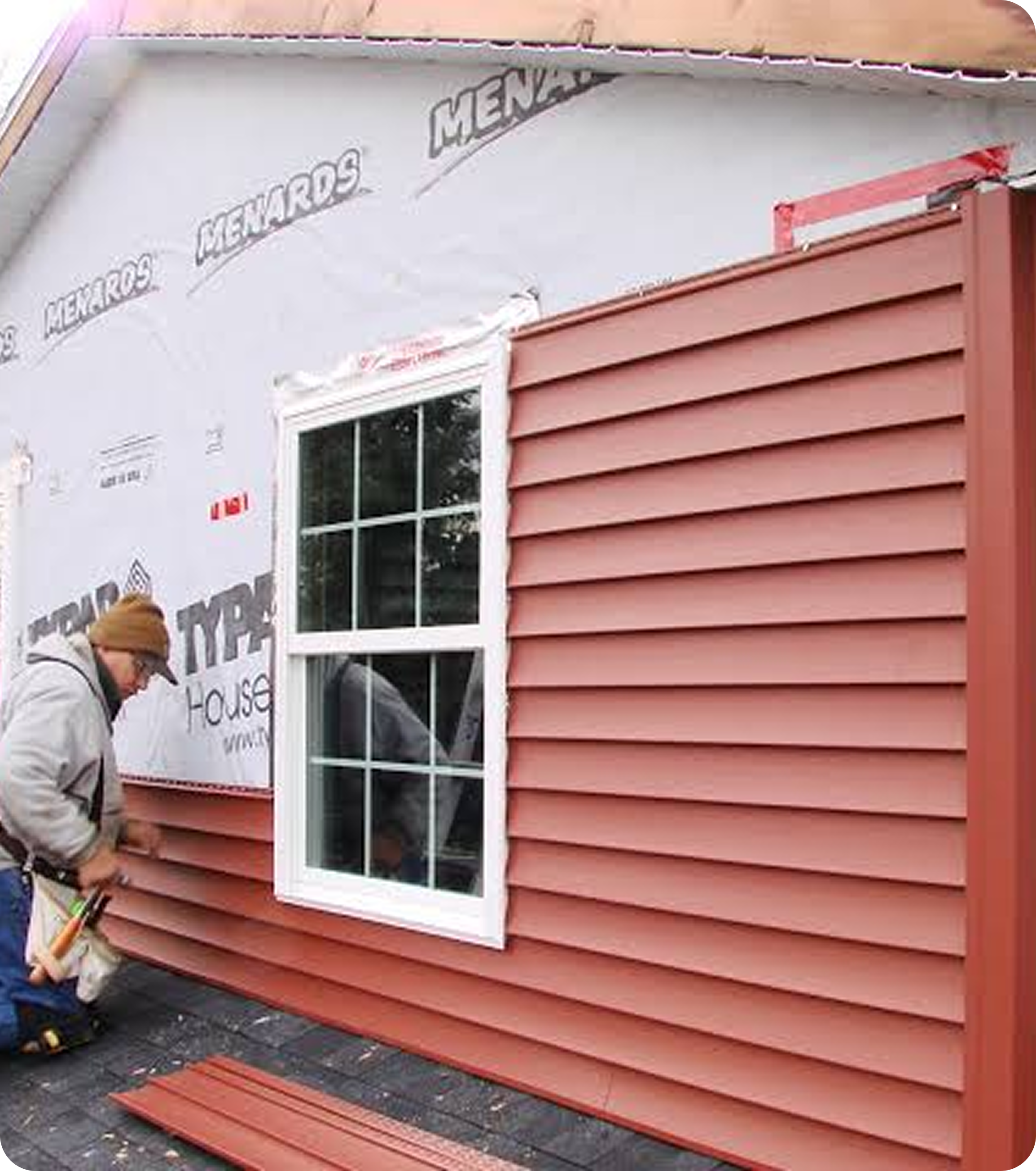 Construction site with pink horizontal siding and a window, workers installing siding, and a sign that reads "Affordable Housing".