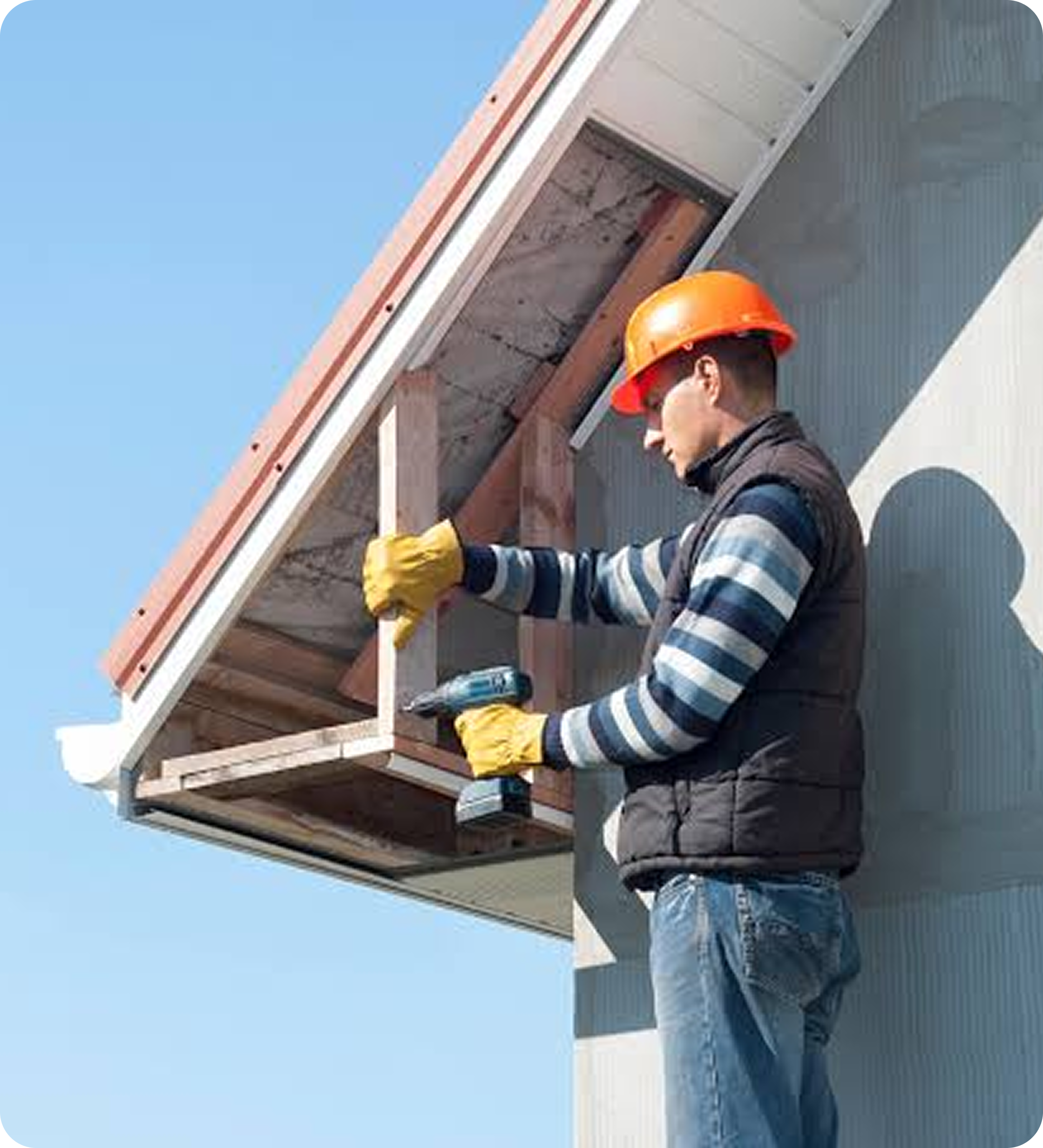 A construction worker in a hard hat and yellow gloves is working on the roof of a building under construction, with a clear blue sky in the background.