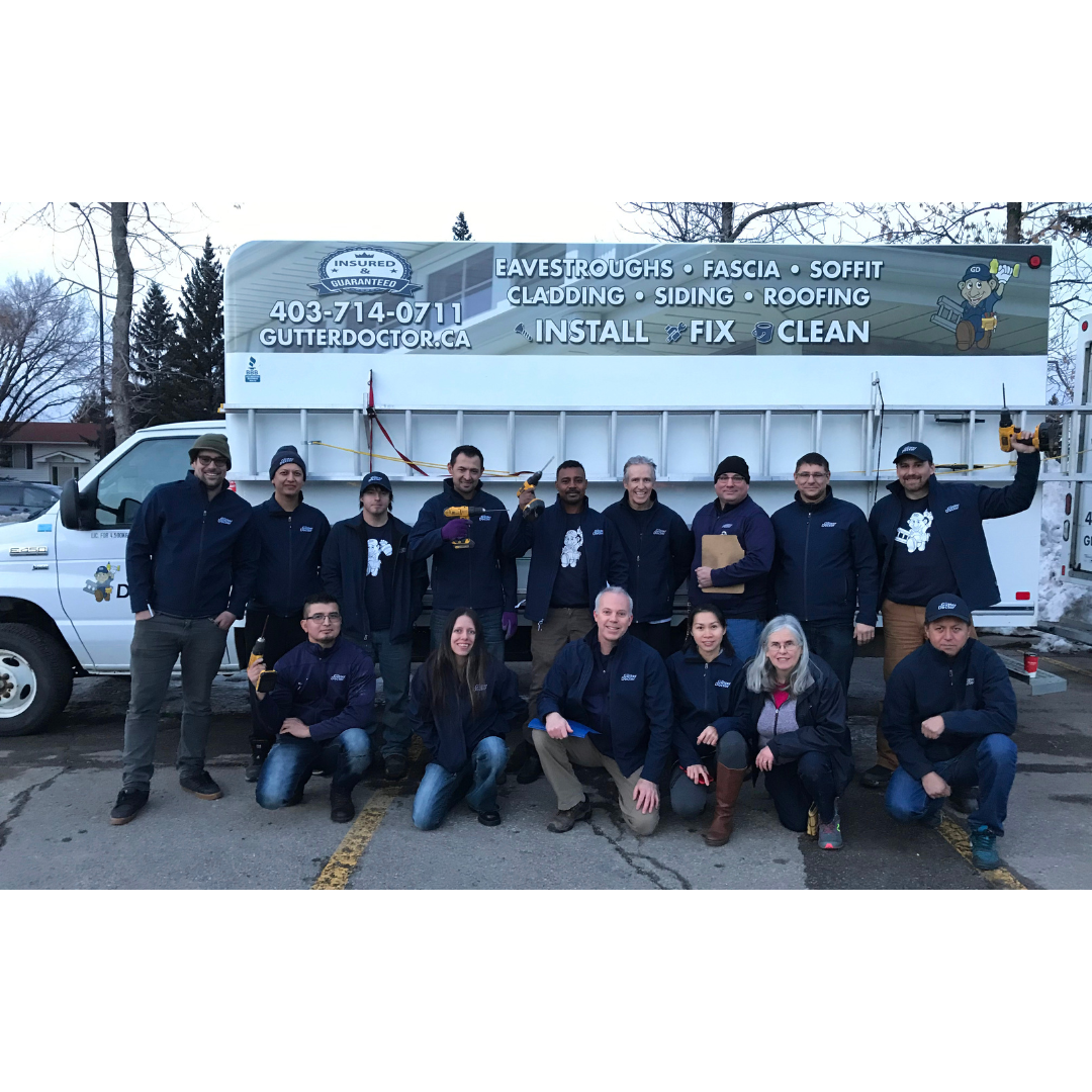 Group of workers standing and kneeling in front of company truck, smiling, with tools, in cold weather.