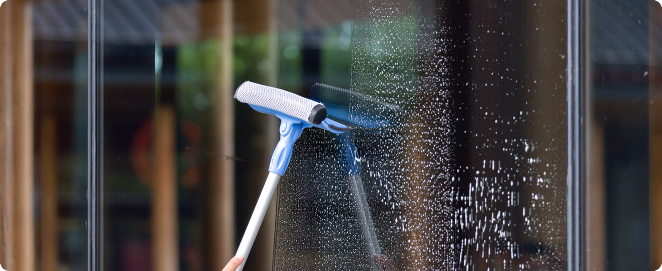 A handheld telescopic squeegee cleaning tool wiping a soapy exterior glass window, leaving a clear section in its path.