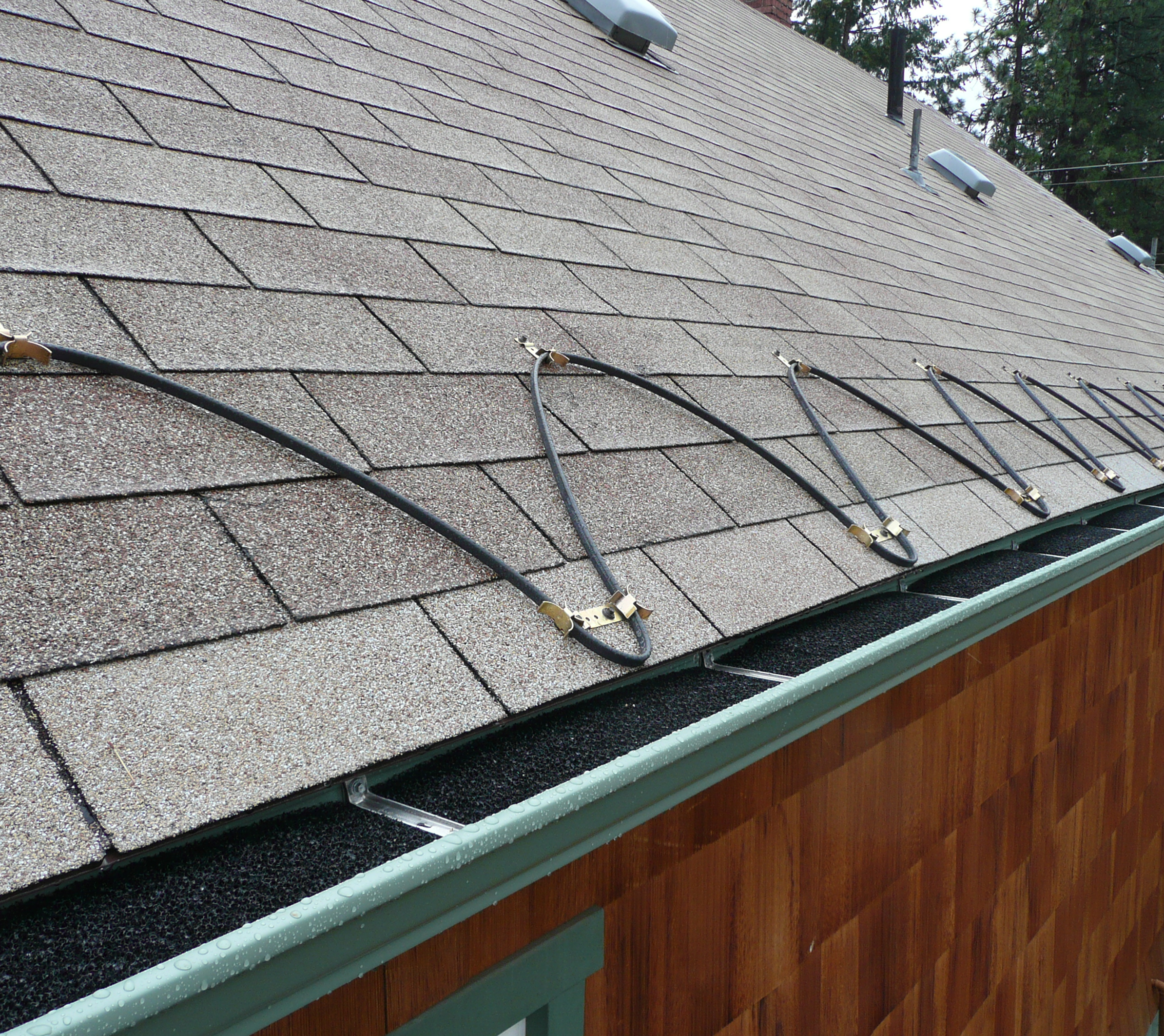 Close-up view of a residential roof with asphalt shingles being replaced, showing roofing tools and materials, with trees in the background.