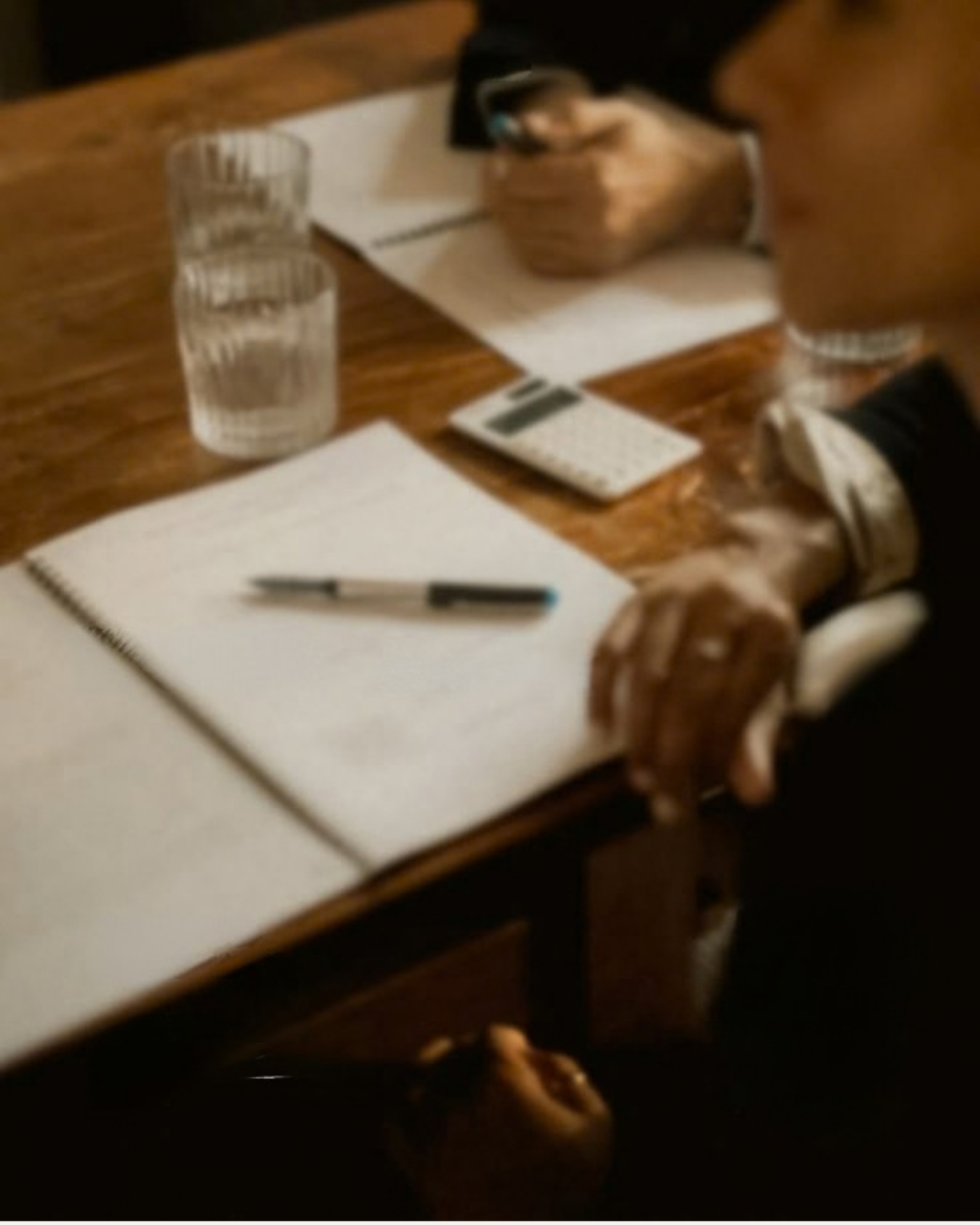 Close-up of a person's hands holding a smartphone over a table with two glasses of water, a notepad, and a pen.