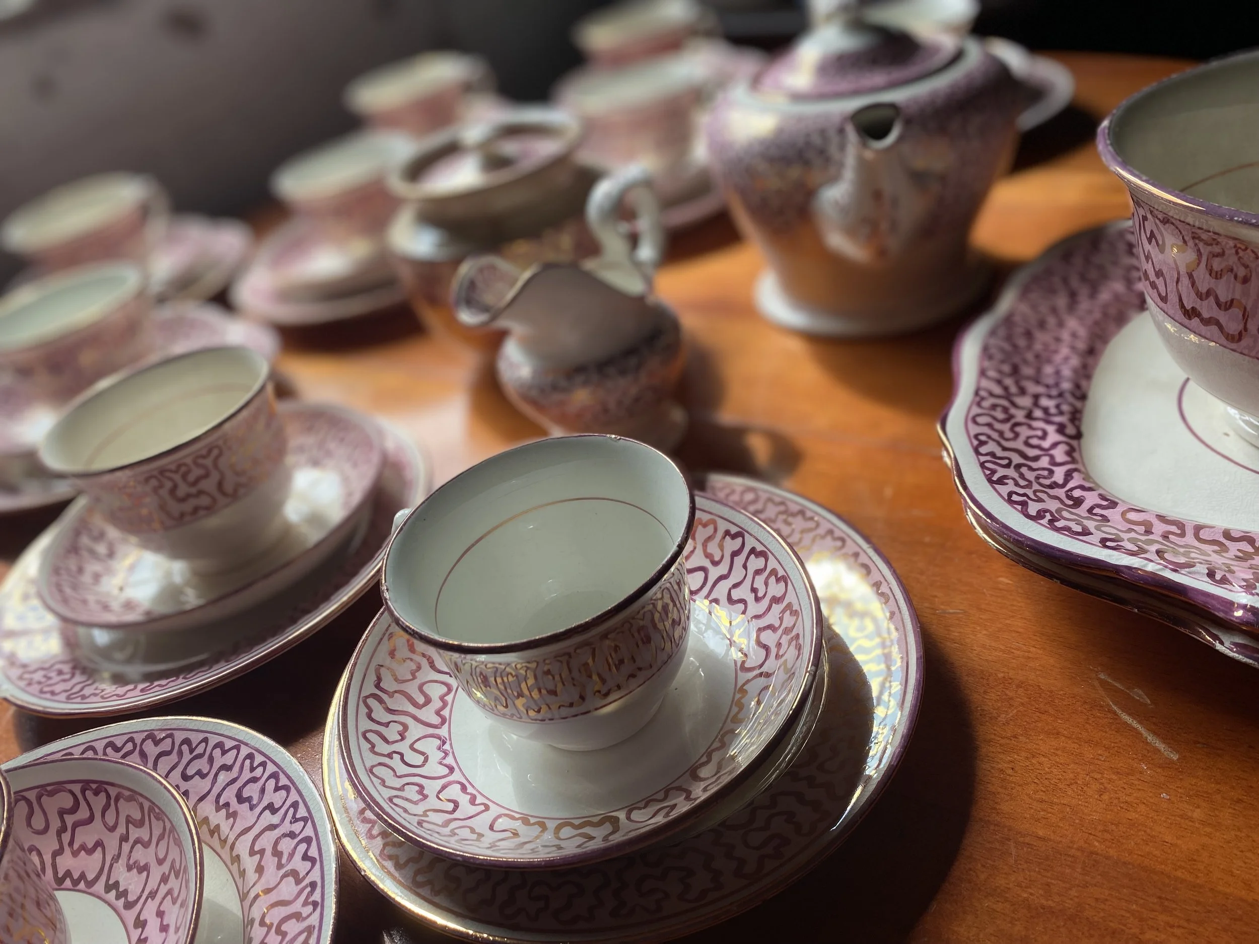 Close-up of a set of pink and purple patterned porcelain tea cups and saucers arranged on a wooden surface.