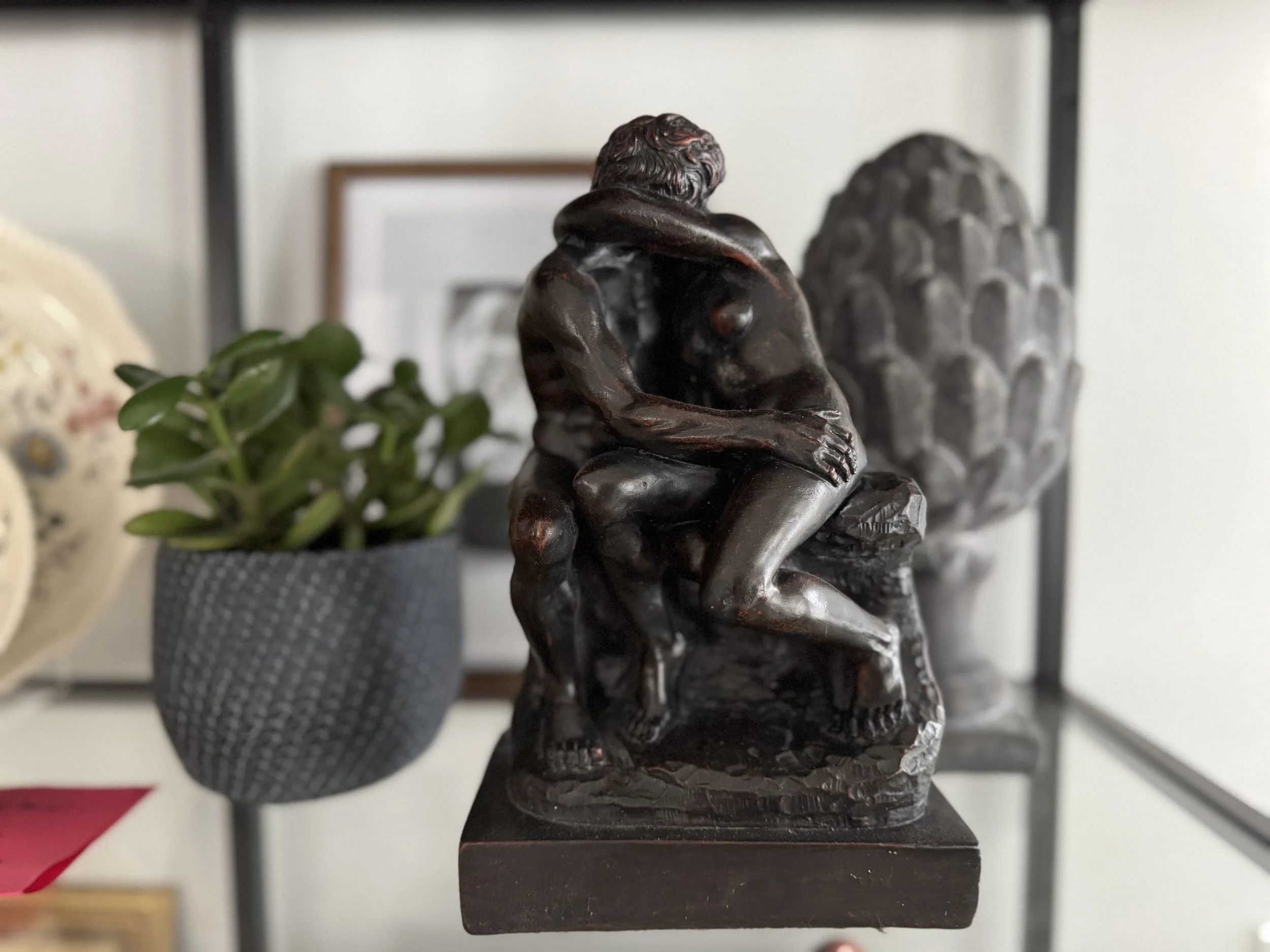 A black sculpture of a seated figure with knees drawn up and head resting on arm, alongside agate or chalcedony stone with textured surface, on a black square base.