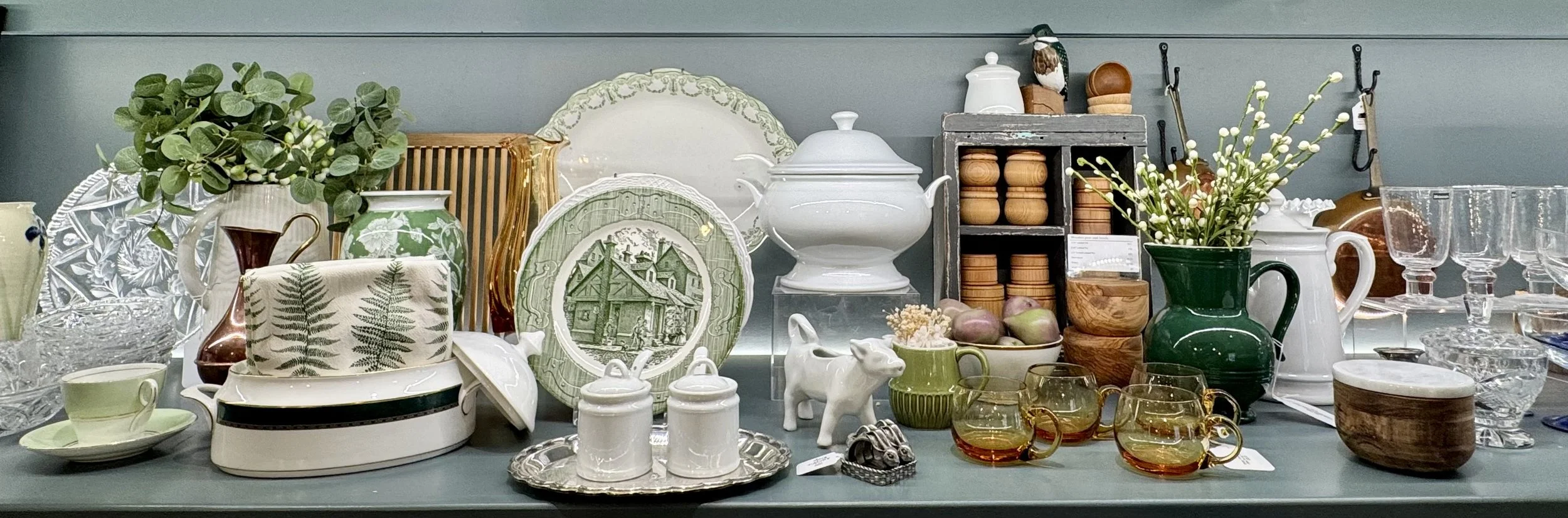 An assortment of vintage and decorative tableware including plates, cups, pitchers, glassware, and small decorative items on a shelf or display.