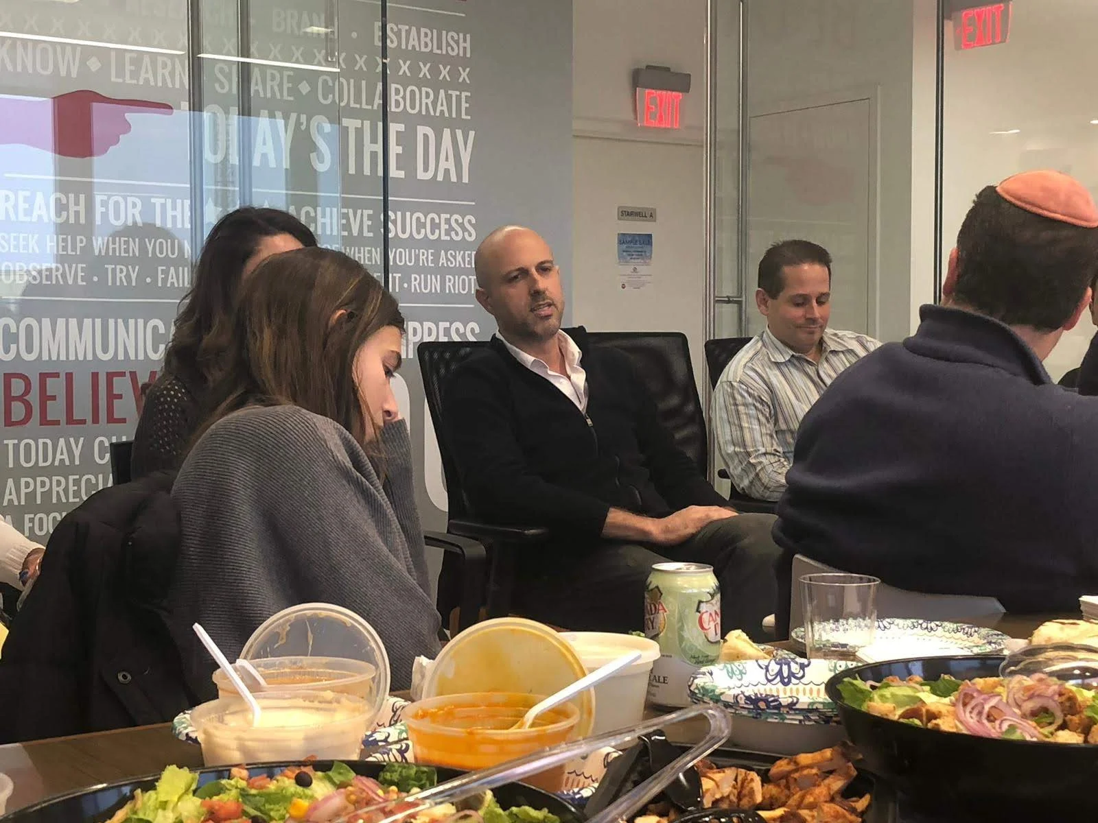 Ari Jason coaching client team seated at a long table during a meeting with motivational words in the background.