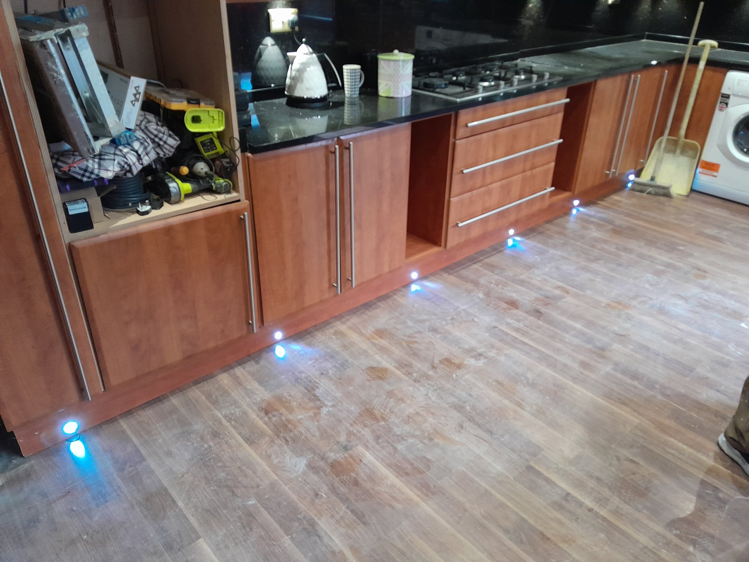 Kitchen with wooden cabinets, black countertops, a stove, and a washing machine; blue LED floor lights.