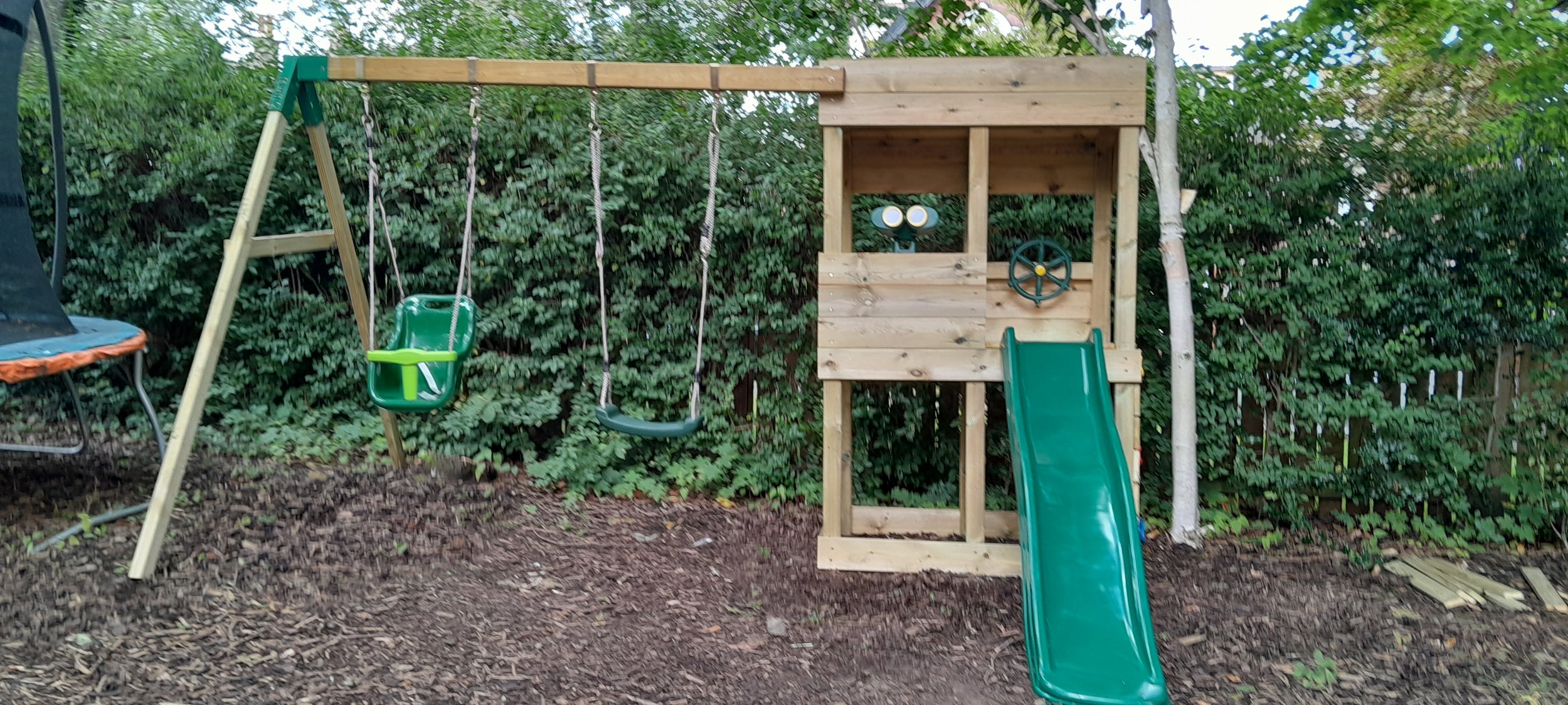 Children's playground set with swings, slide, and playhouse in a backyard.