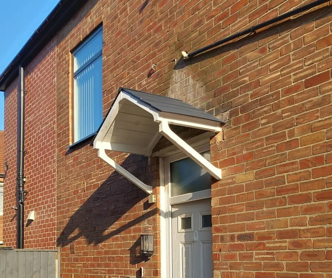 House exterior with brick wall, window, and white front door with overhanging porch canopy.