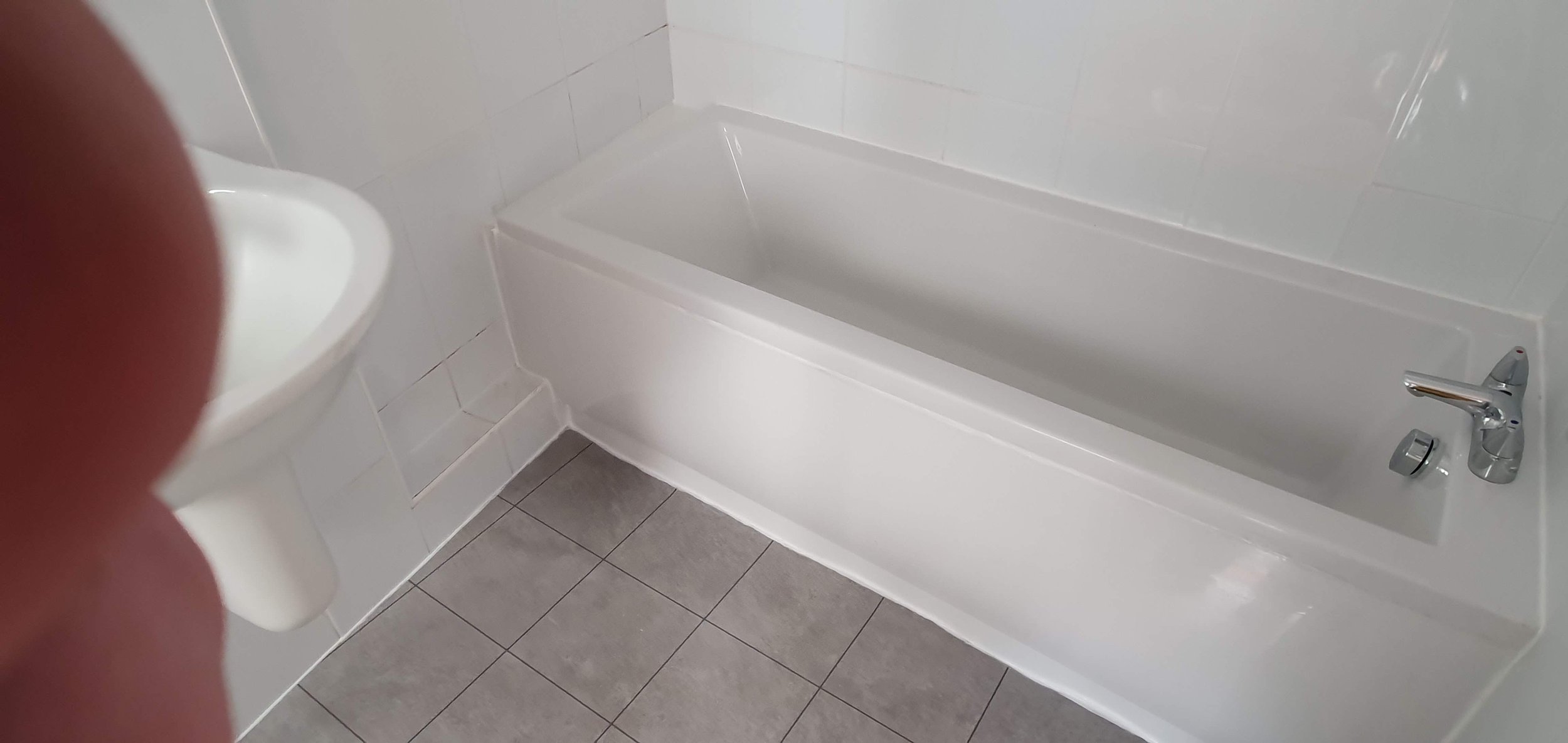 Bathroom with white bathtub, sink, and gray tiled floor.
