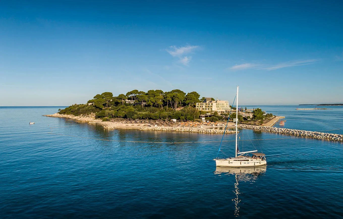 Sailboat near a coastal island with trees and buildings