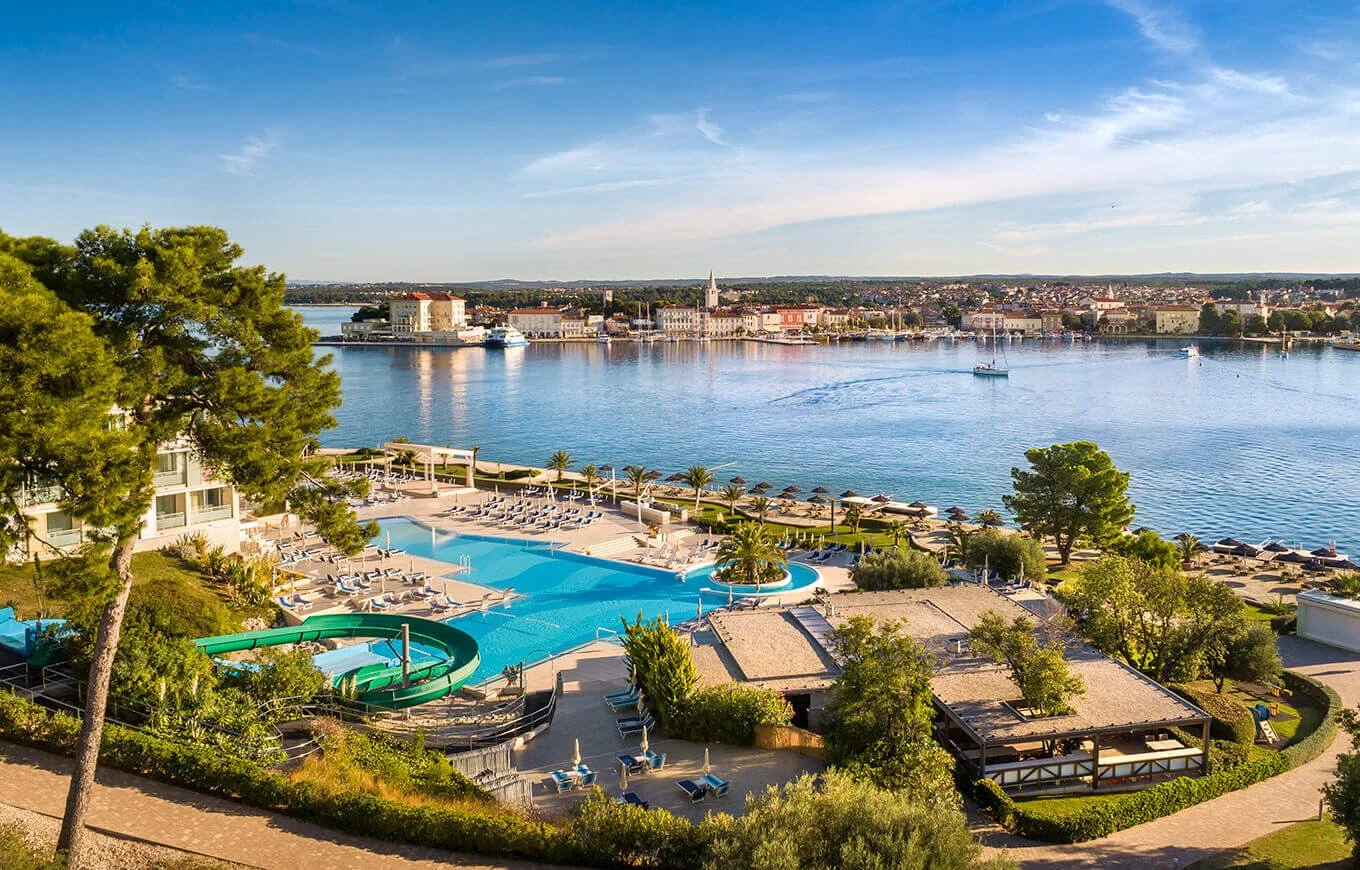 Waterfront resort with pools, surrounding greenery, and buildings across the water.