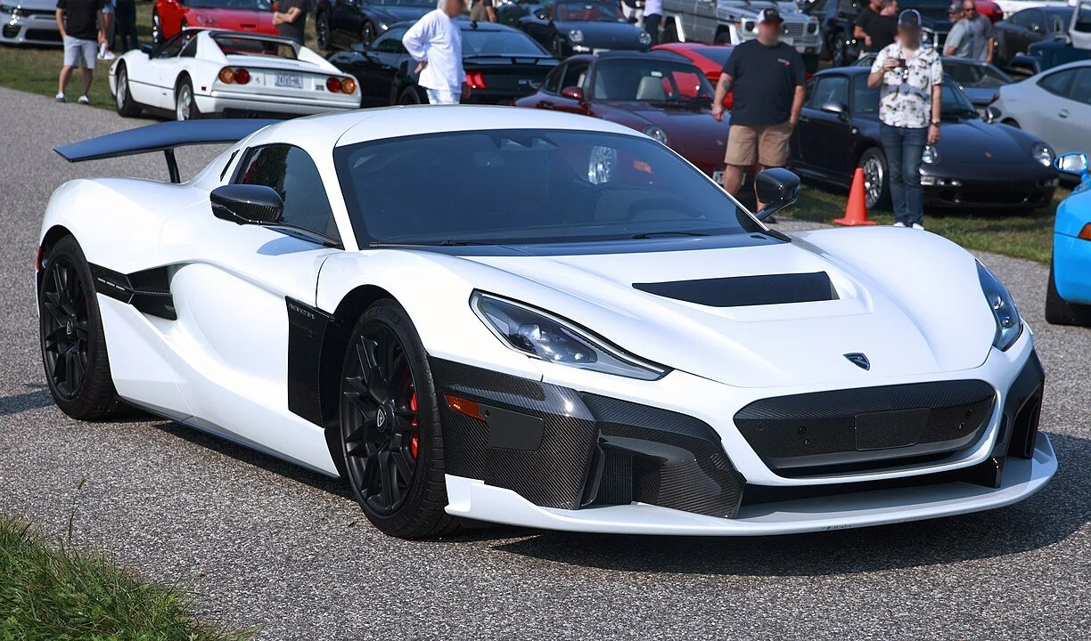 Weißer Rimac Nevera bei einem Autotreffen in Bridgehampton, fotografiert von vorne rechts – vollelektrischer Hypercar mit Carbon-Details und markanter Aerodynamik.