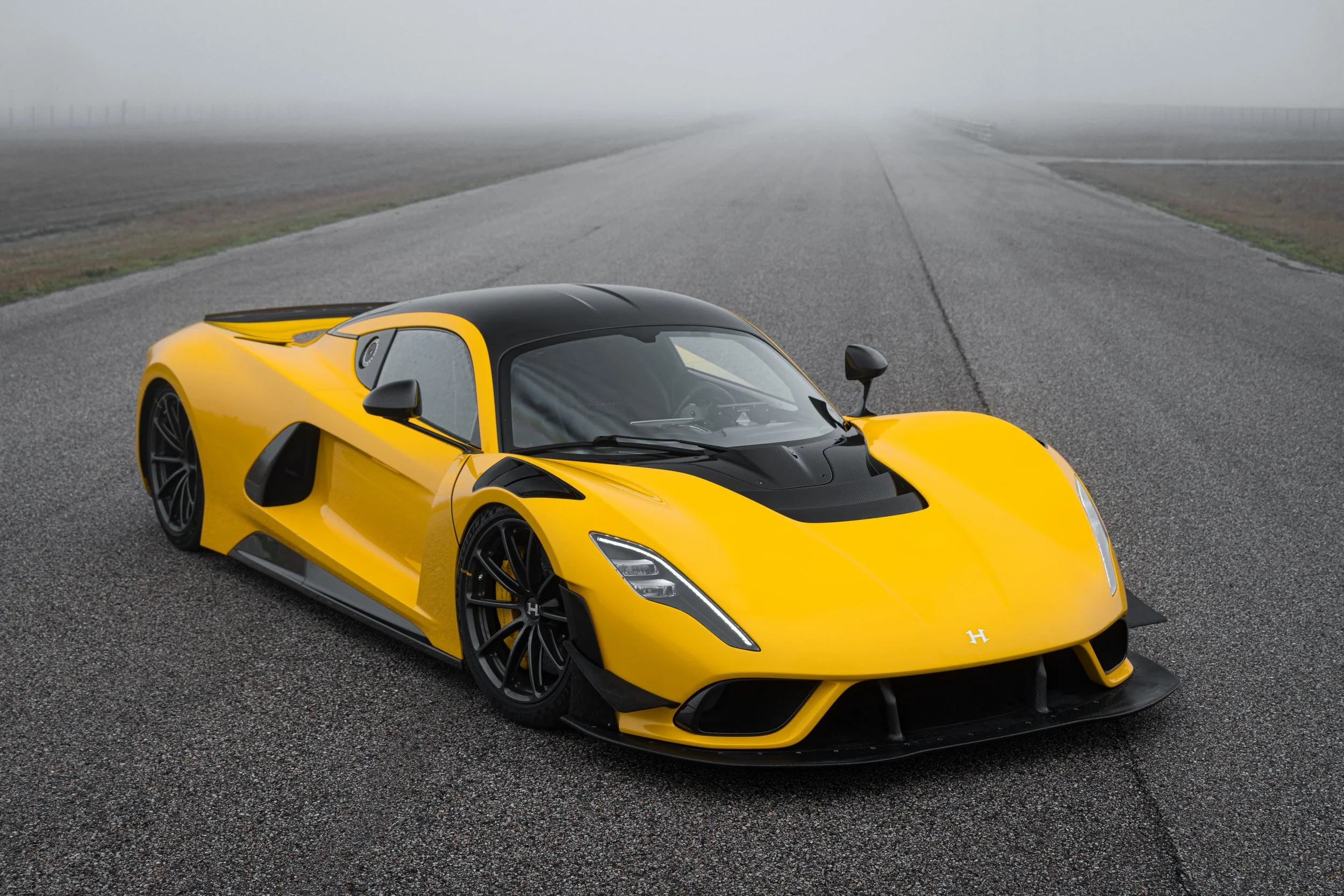 Gelber Hennessey Venom F5 Evolution Hypercar mit schwarzem Dach auf nebliger Teststrecke, Front- und Seitenansicht, leistungsstärkstes Verbrenner-Supersportfahrzeug der Welt.