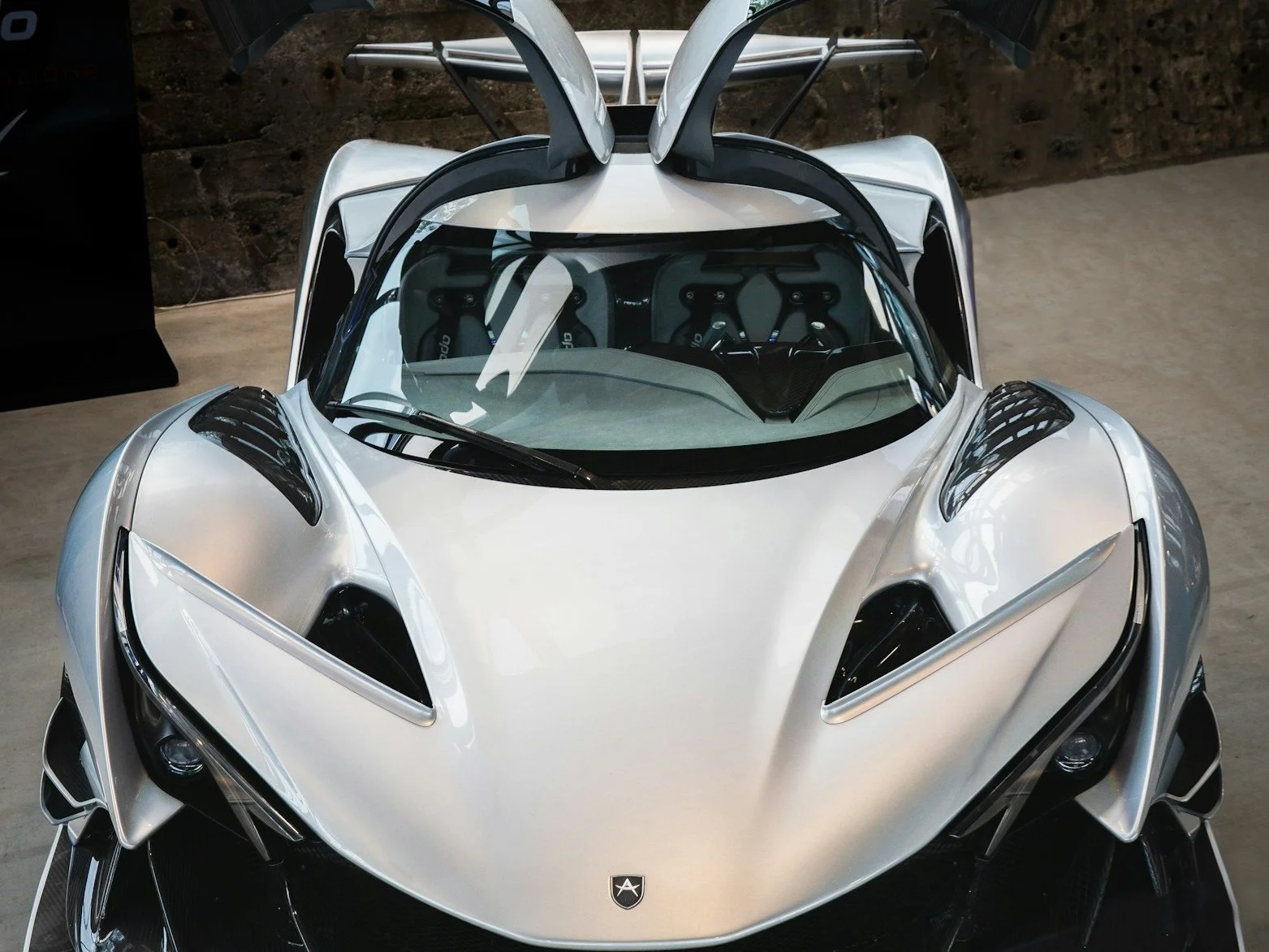 Der Apex AP-0 aus der Frontperspektive – futuristisches Hypercar mit aerodynamischem Design, sichtbaren Kohlefaserelementen und offener Sicht auf das Cockpit.