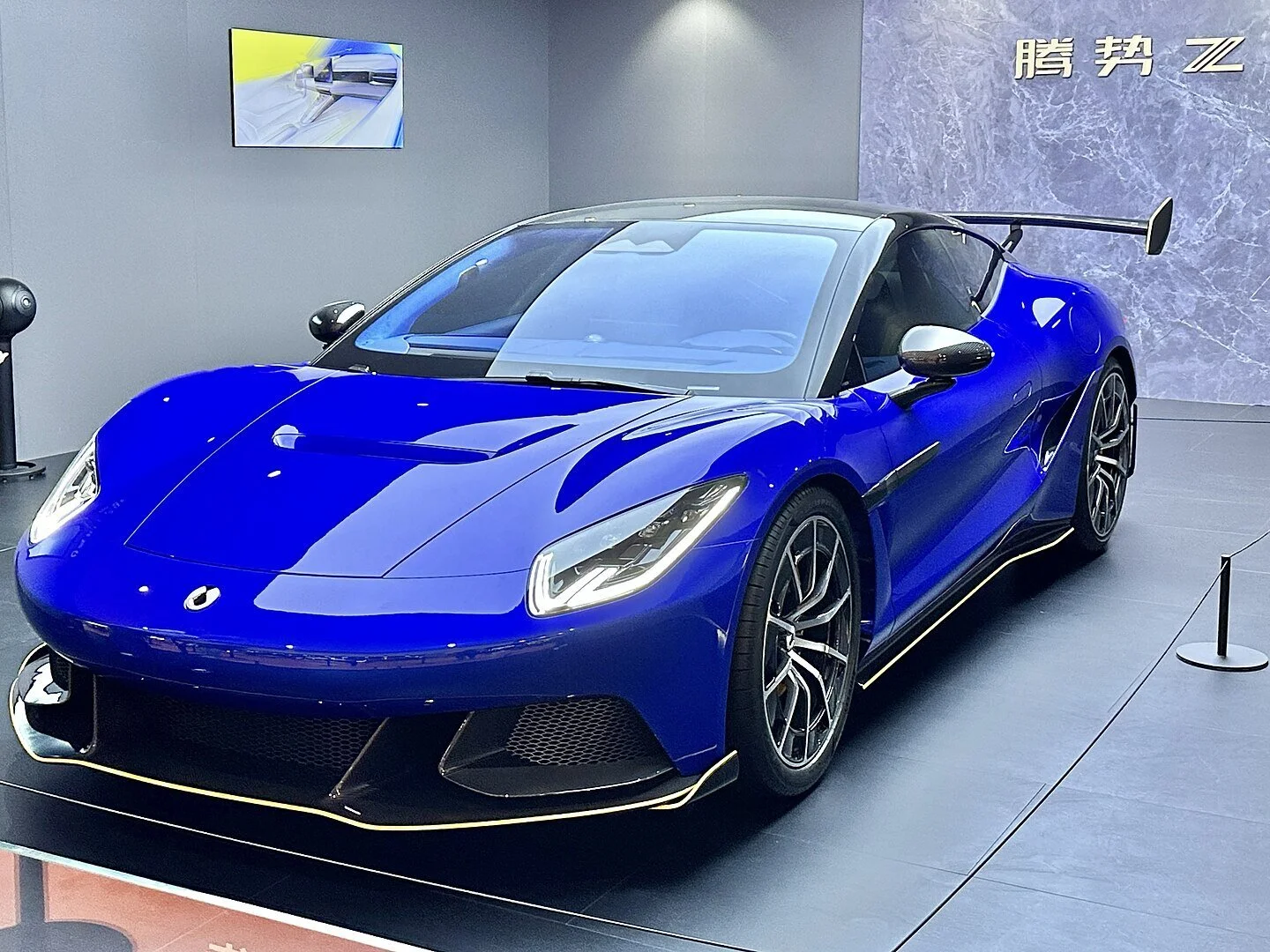 Blauer Denza Z Supersportwagen mit markantem Heckflügel auf Automesse, seitlich-frontal aufgenommen, chinesischer Elektro-Hypercar mit aerodynamischem Design und futuristischer Linienführung.