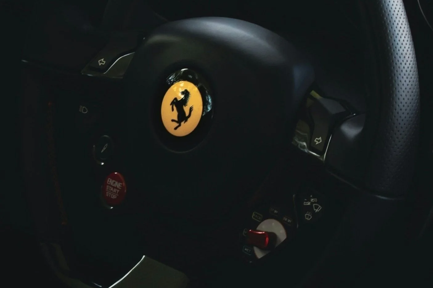 Fersengriff mit Ferrari-Logo in einem Autositz, rote Start-Stopp-Taste, multifunktionale Steuerelemente am Lenkrad.