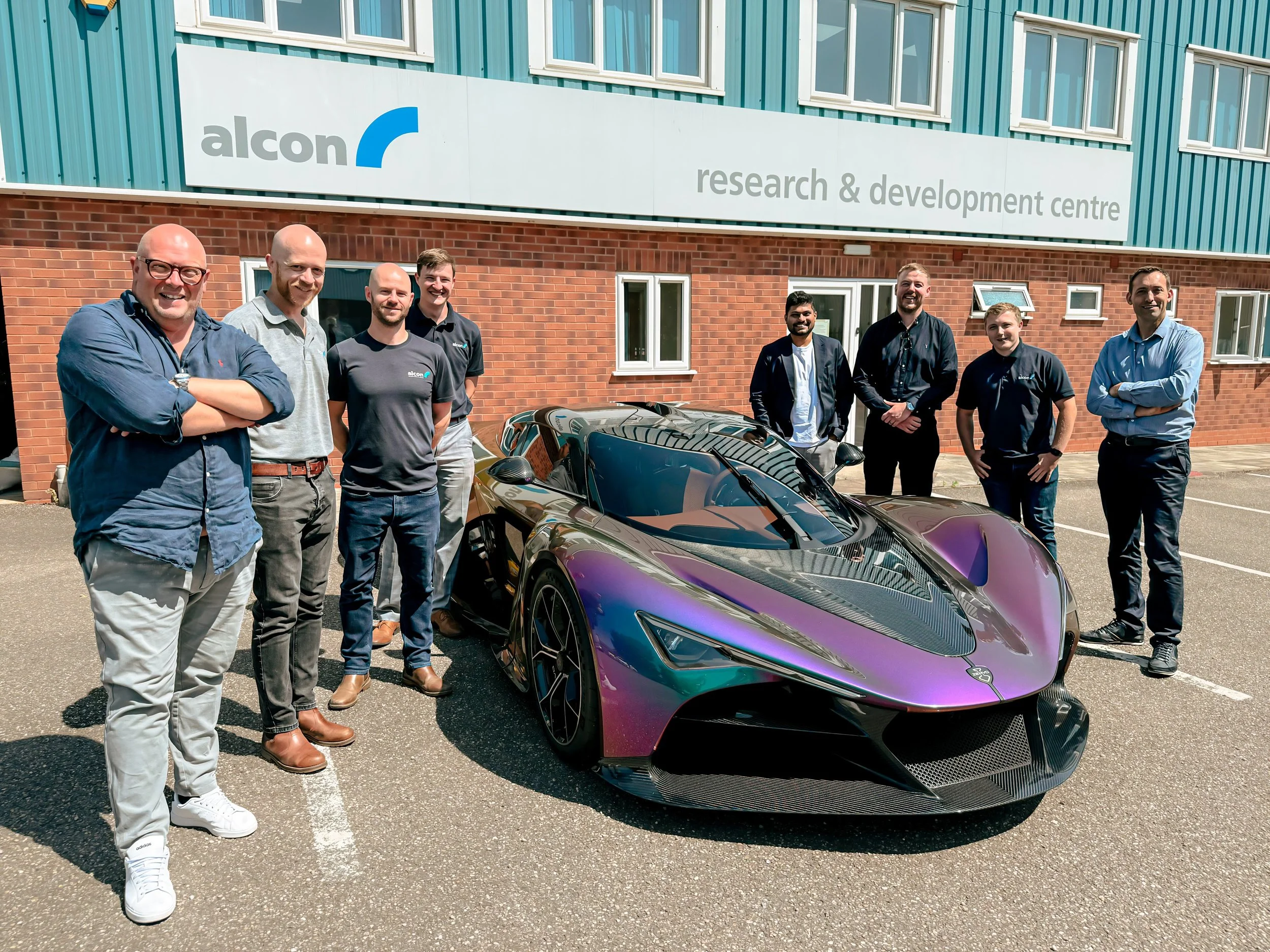 Die Zenvo Aurora im changierenden Lack vor dem Alcon Forschungs- und Entwicklungszentrum, umgeben vom Zenvo- und Alcon-Entwicklungsteam nach Bekanntgabe der technischen Partnerschaft für Hochleistungsbremsen.