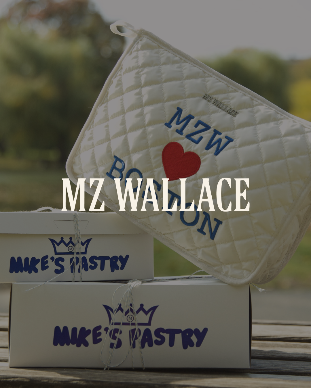 A quilted white golf visor with blue and red embroidery that says "MZ Wallace Boston" and a red heart. Below, two white boxes with blue lettering saying "MIKE'S PASTRY" are stacked on a wooden surface.
