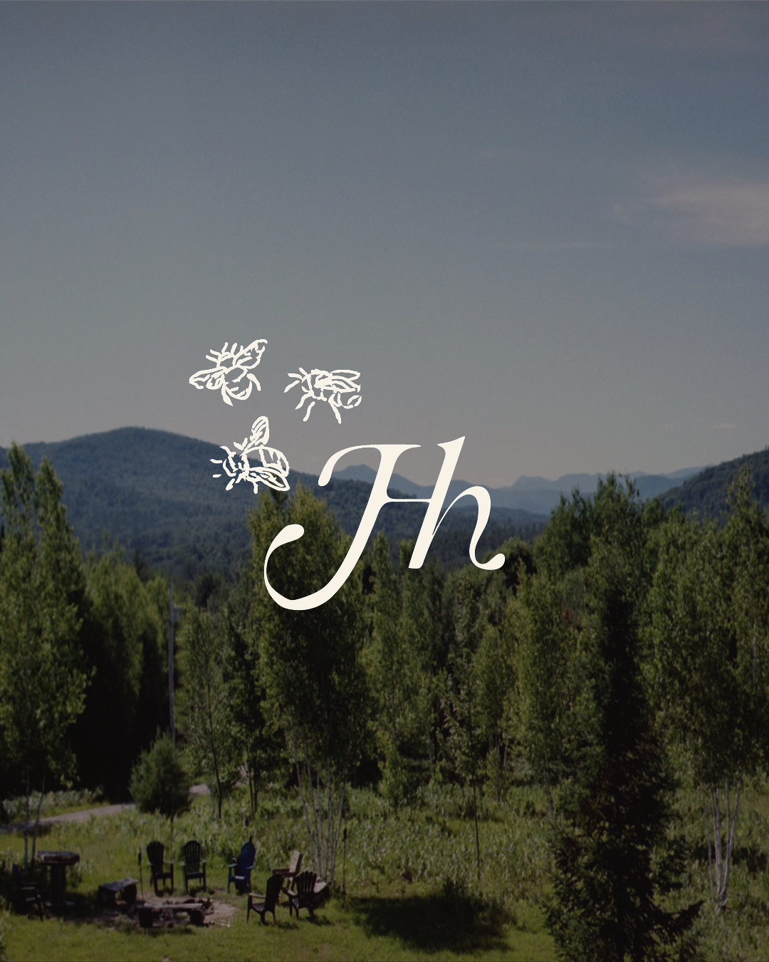 Scenic view of a mountain landscape with green trees and a few Adirondack chairs arranged around a fire pit, under a cloudy sky, with a logo of bees and the initials 'Jh' overlaid.