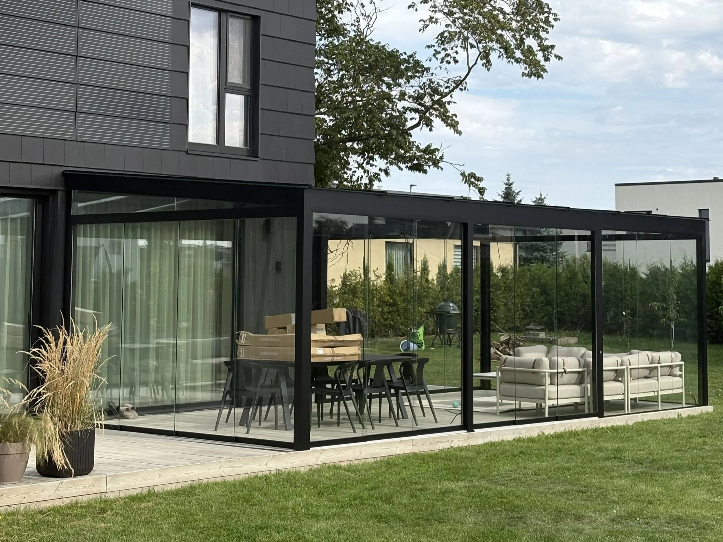 Täysin lasitettu terassi modernilla sisustuksella ja vihreällä pihalla.
