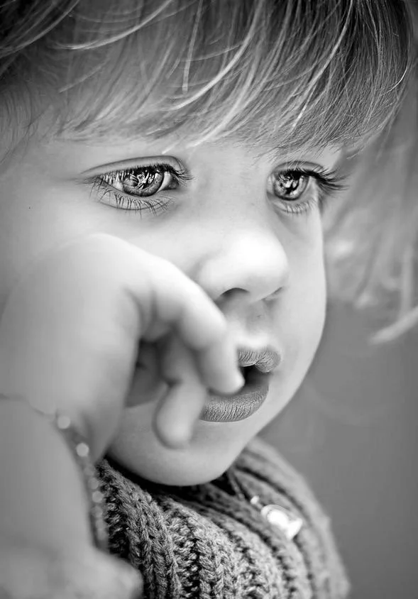 Un gros plan d'une jeune fille en noir et blanc, observant pensivement avec ses mains près du visage.