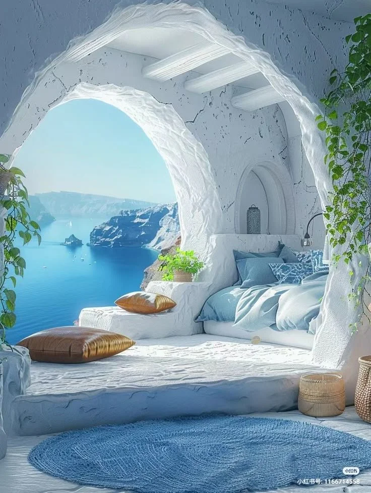 Intérieur d'une pièce blanche avec vue sur la mer et des falaises, mobilier en style naturel, plantes vertes, coussins bleus et une tapis bleu