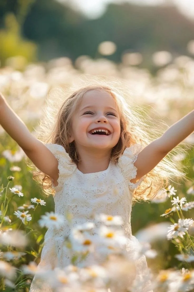Fille souriante avec les bras levés dans un champ de marguerites en plein air, soleil brillant.