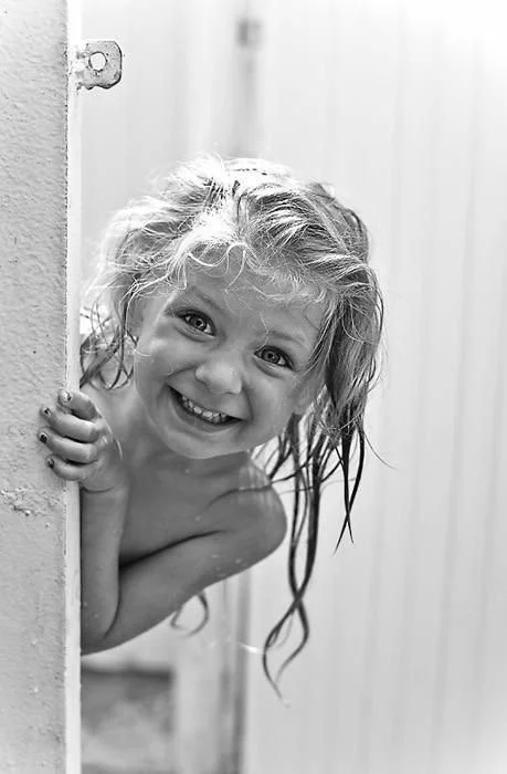 Une jeune fille souriante avec les cheveux mouillés, tenant une porte, dans un intérieur en bois.