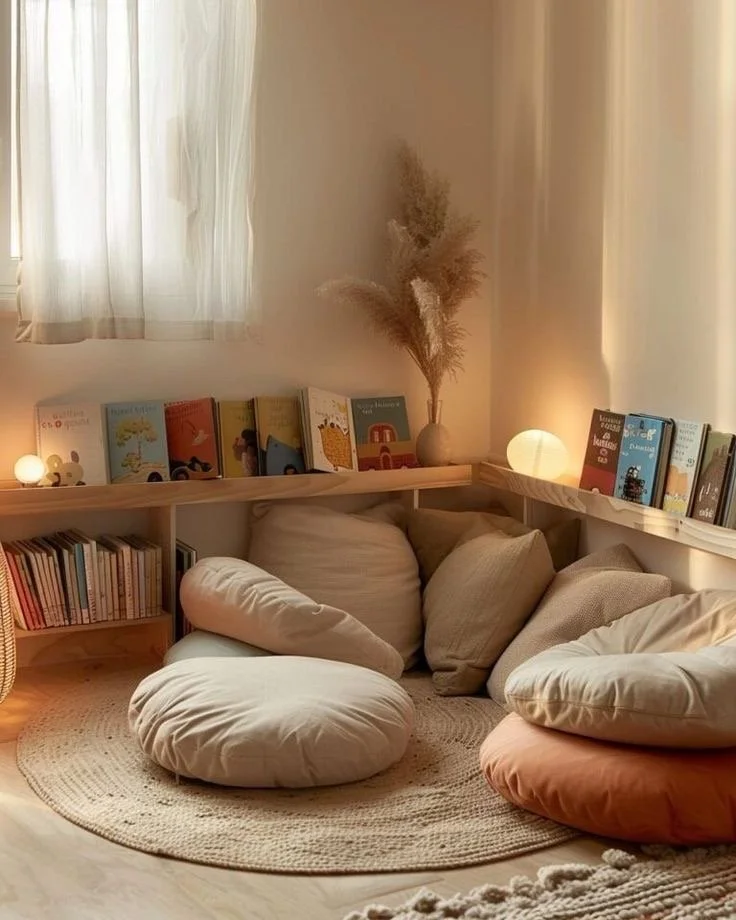 Coin lecture cosy avec coussins, livres pour enfants, lampes douces et décoration naturel avec des pampas dans un coin de pièce.
