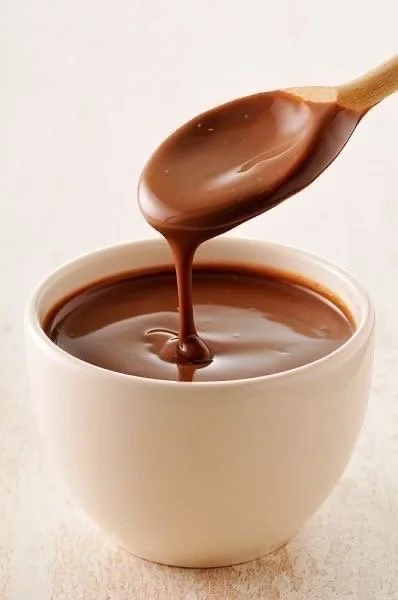 Cuillère en bois versant du chocolat fondu dans un bol blanc