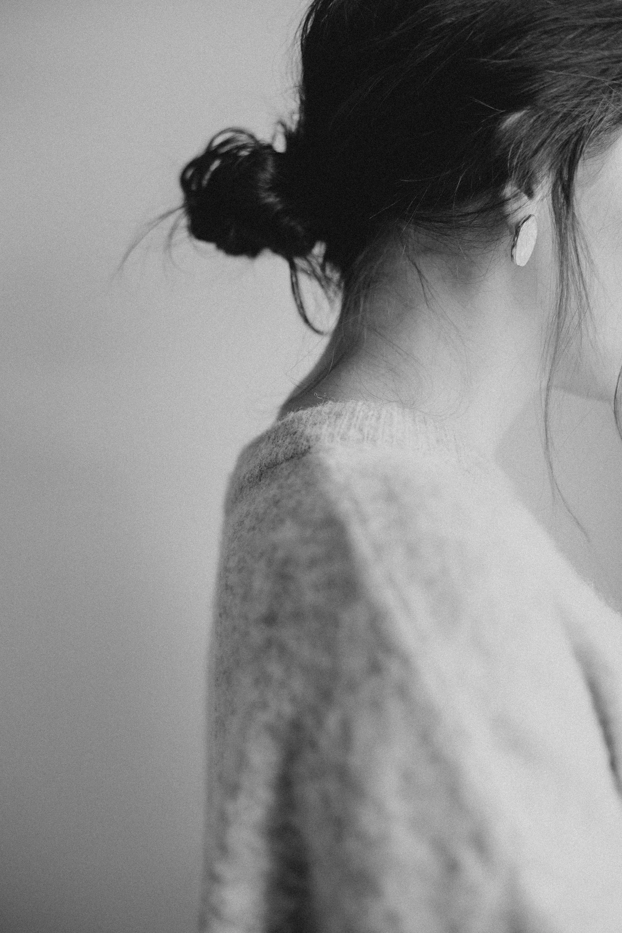 Black and white image of a woman with her hair tied in a messy bun, wearing a cozy knit sweater, highlighting an earring.